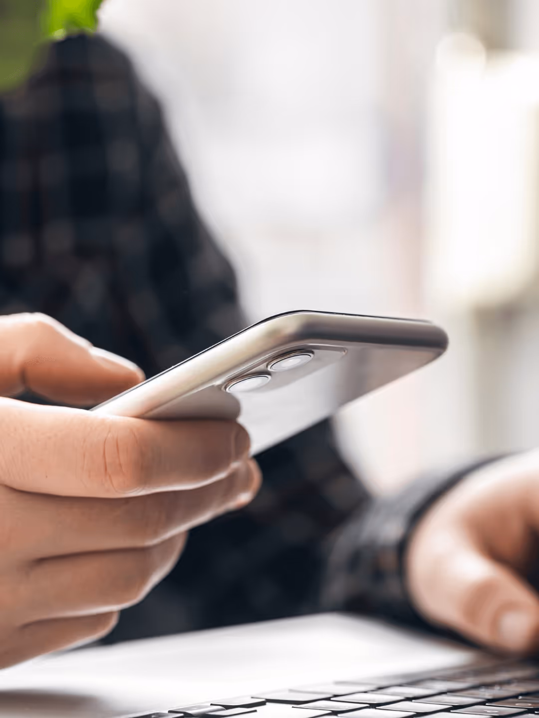Person hält Smartphone über Tisch mit Laptop und Kaffeetasse