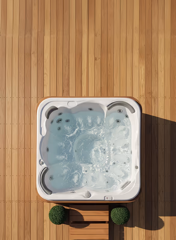 Top-down view of a bubbling white hot tub on a wooden deck with two green round shrubs on either side of wooden steps.