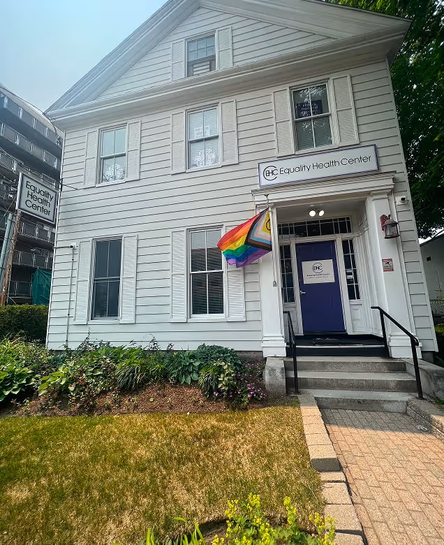 White two-story building housing BHC Equality Health Center with a rainbow pride flag displayed near the entrance.
