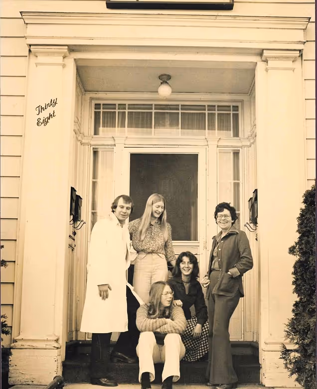 Five people posing on the steps in front of a house entrance with 'Thirty Eight' written on the left pillar, black and white photo with sepia tone.