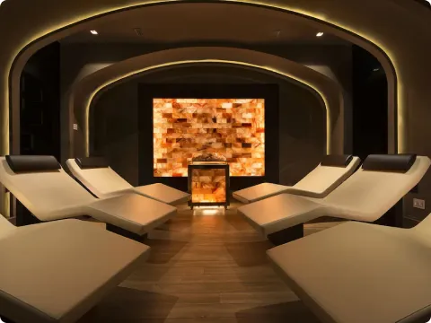 Stanza rilassante con sei lettini bianchi su pavimento in legno e parete illuminata da luci calde e pannello decorativo retroilluminato.