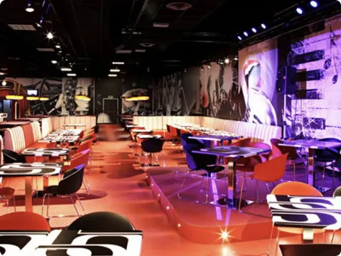 Interno di un ristorante moderno con sedie colorate, tavoli con tovagliette astratte e pareti decorate con murales.