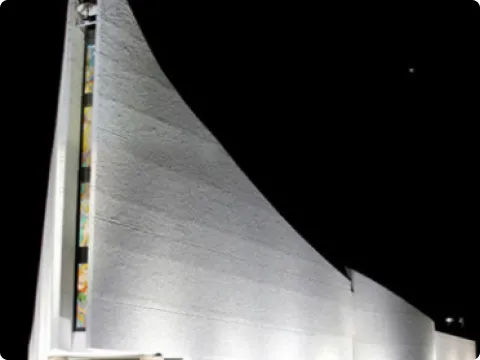 Struttura architettonica illuminata di bianco con pareti curve contro un cielo notturno scuro.