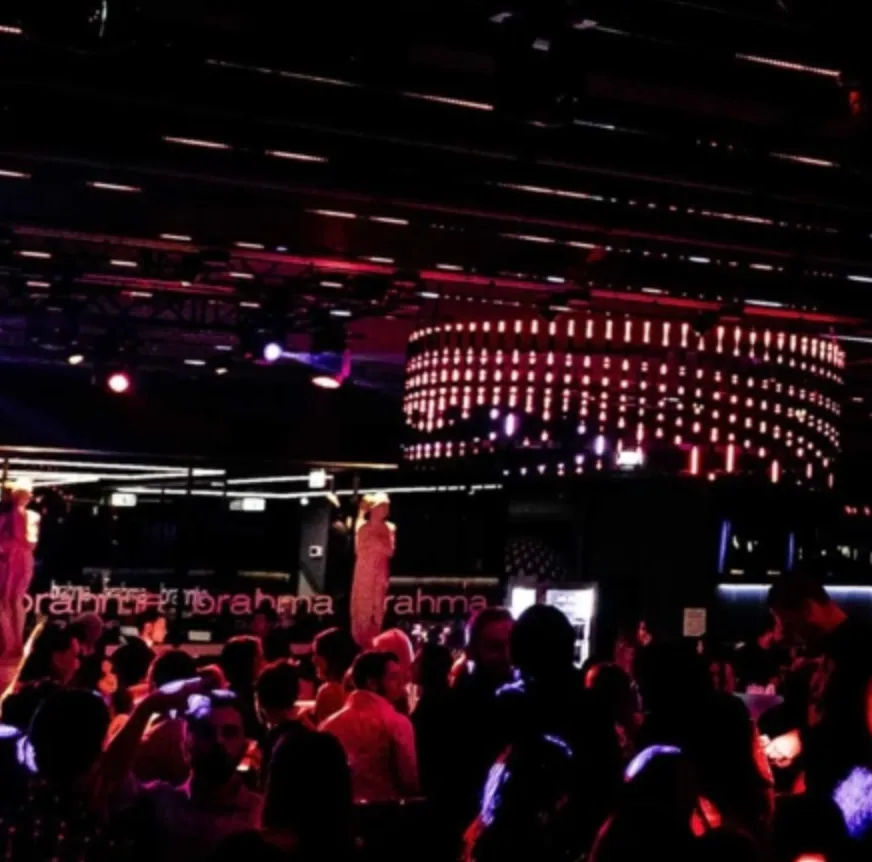 Folla di persone in un locale notturno con luci rosse e lampadario luminoso al soffitto.