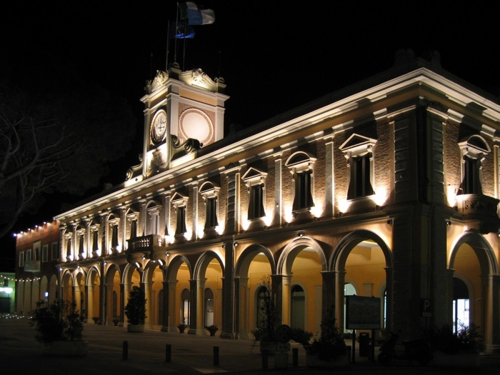 Edificio storico illuminato di notte con archi al piano terra e orologio sulla torre centrale.