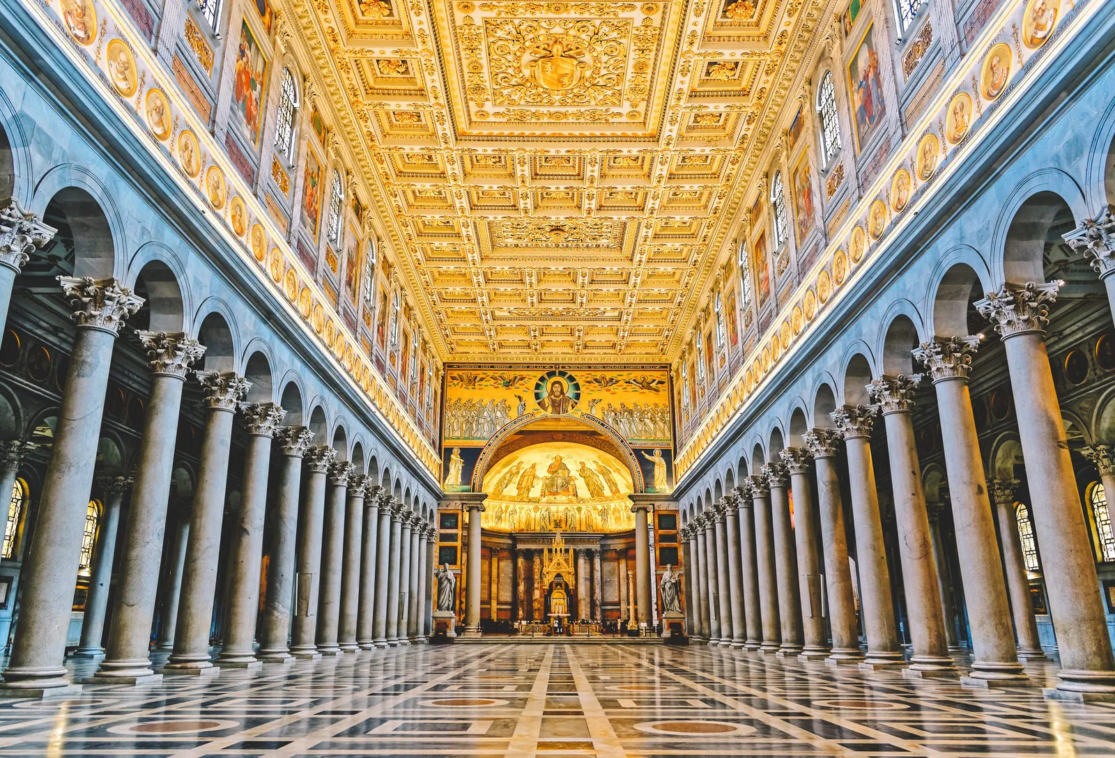 Interno della Basilica di San Paolo fuori le Mura a Roma con ampio colonnato e soffitto decorato dorato.
