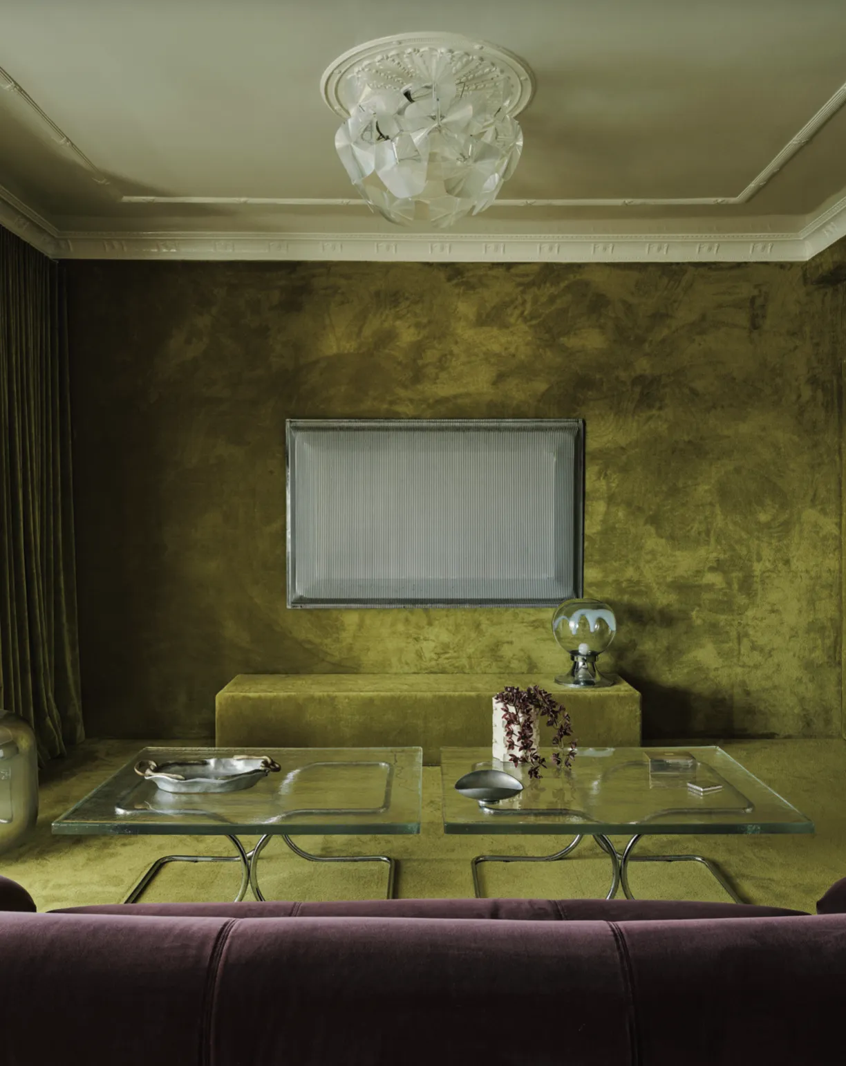 Interno di un moderno bar con tavolo rotondo e quattro sedie verdi, grande quadro colorato sulla parete e scaffali con prodotti e bottiglie.