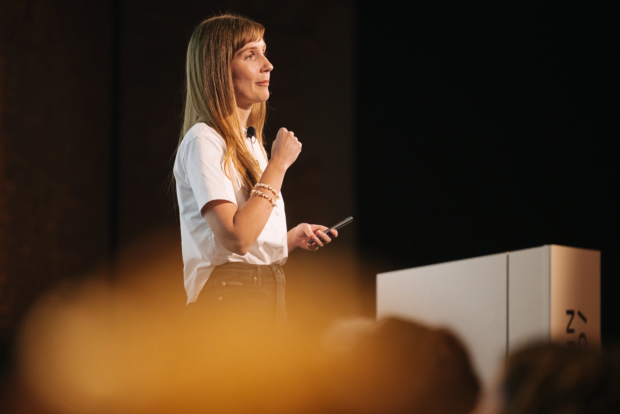 Viola speaking at a conference. She is wearing a white shirt. The background is dark