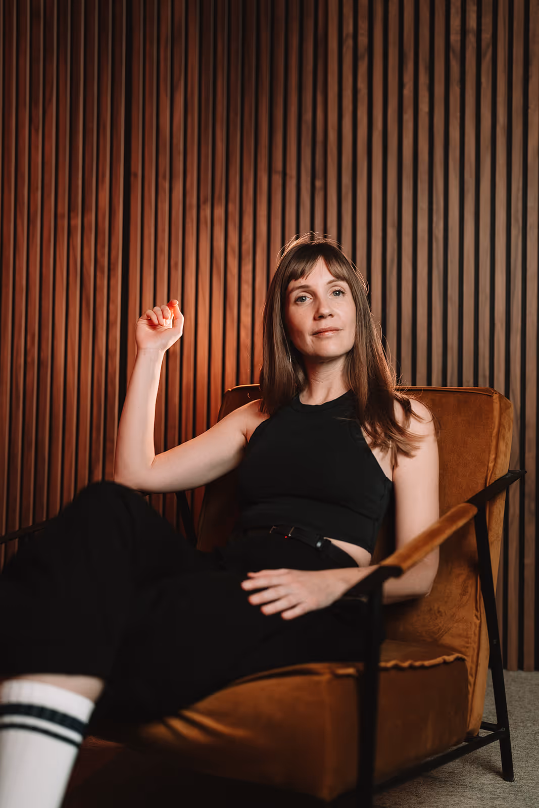 Viola with long brown hair sitting on a brown armchair against a vertical wooden panel wall.