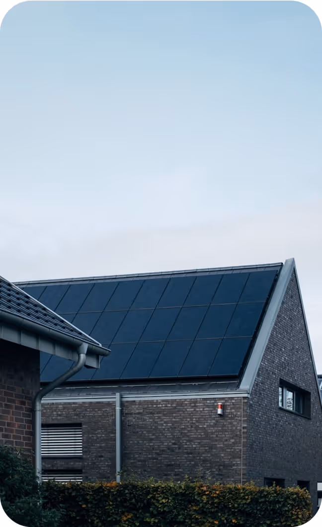 Toit incliné d'une maison en briques avec des panneaux solaires noirs sous un ciel clair.