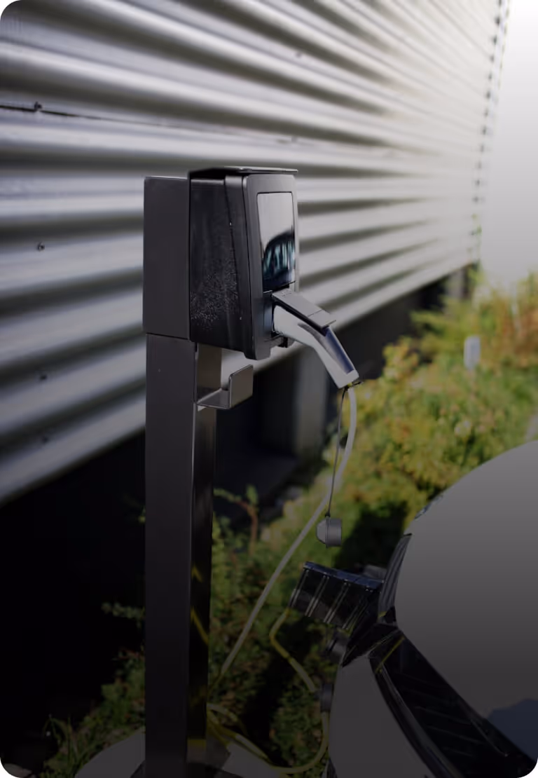 Borne de recharge électrique connectée avec un câble branché sur une voiture stationnée à l'extérieur près d'un bâtiment.
