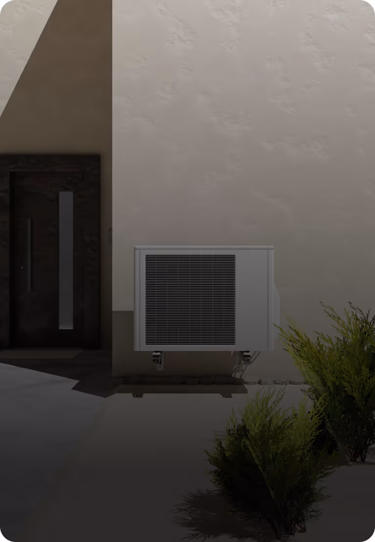 Unité extérieure de climatisation murale montée à l'extérieur d'une maison près d'une porte noire et de buissons verts.