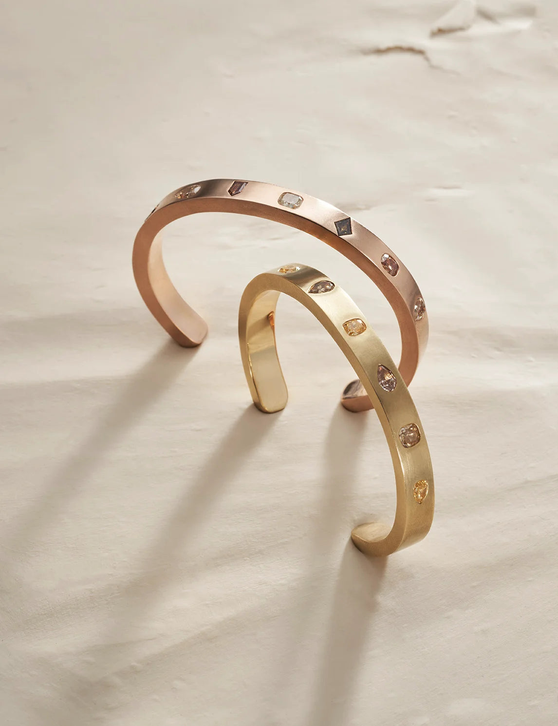 Two gold bangles on a light clay background.