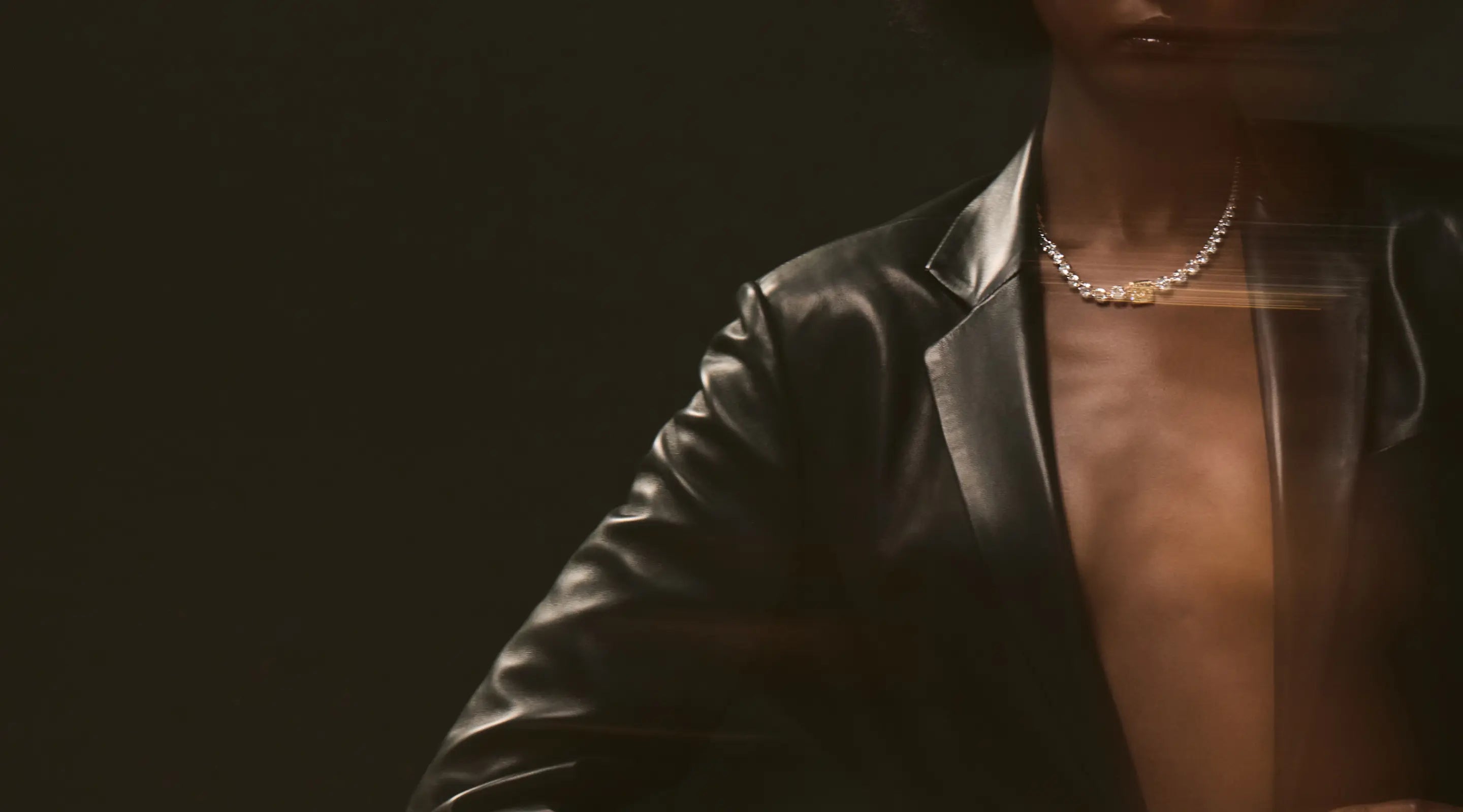 Blonde woman with slicked-back hair wearing a black strapless top and a choker necklace with a large light blue gemstone.