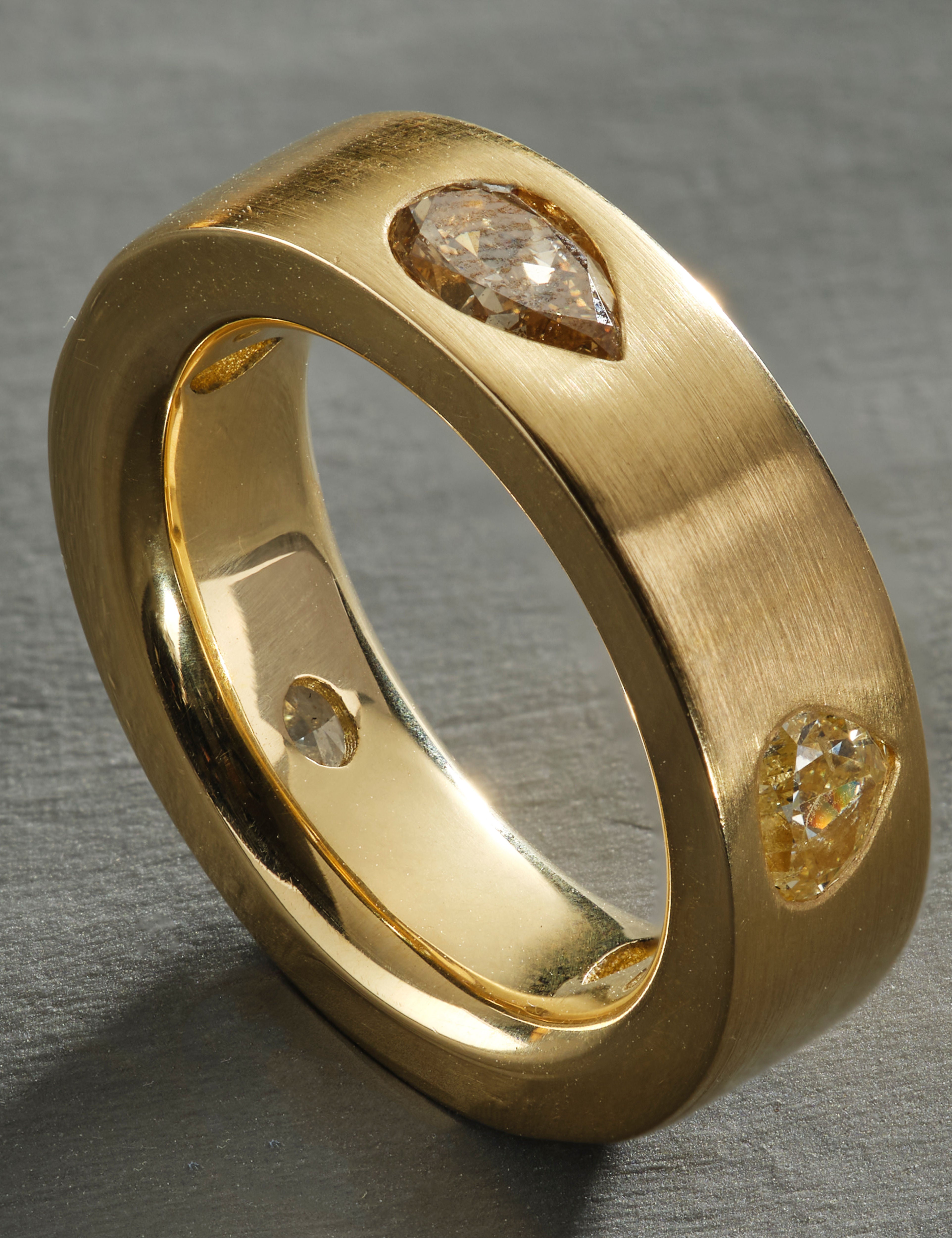 Yellow gold ring featuring pear-cut and round diamonds on matte surface.