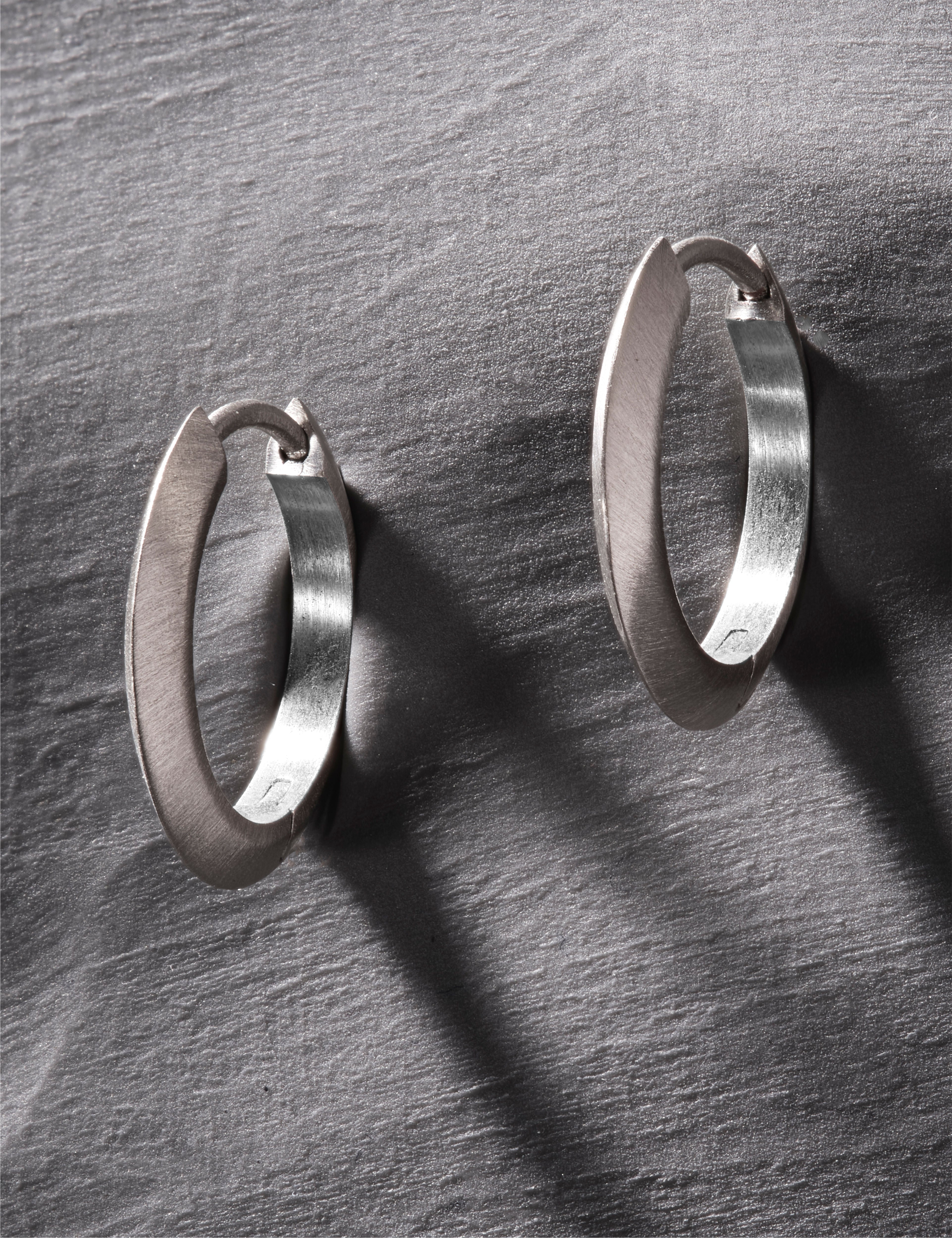 Brushed platinum oval hoop earrings with soft matte finish on grey background.