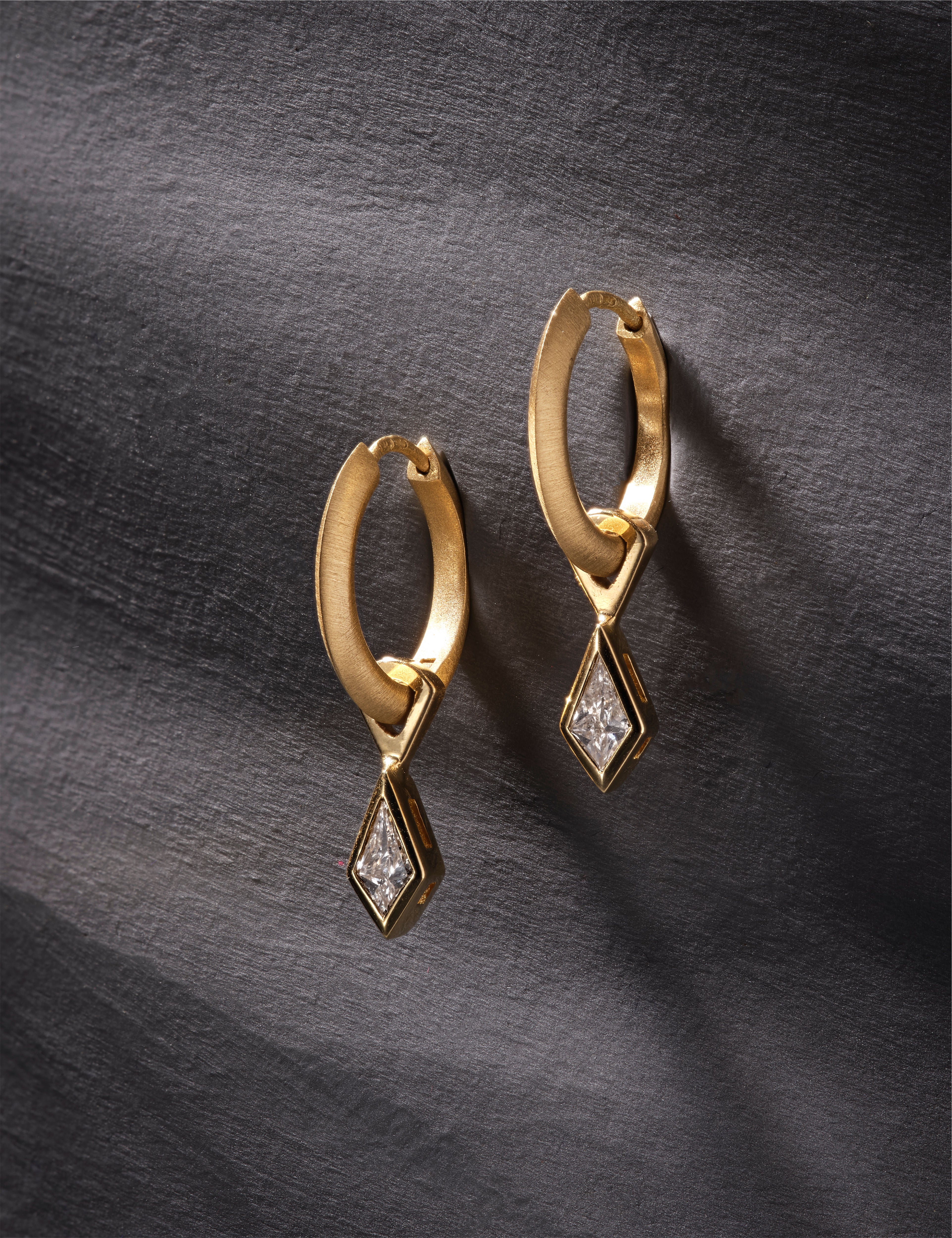 Yellow gold hoop earrings featuring kite-cut diamonds on dark textured surface.