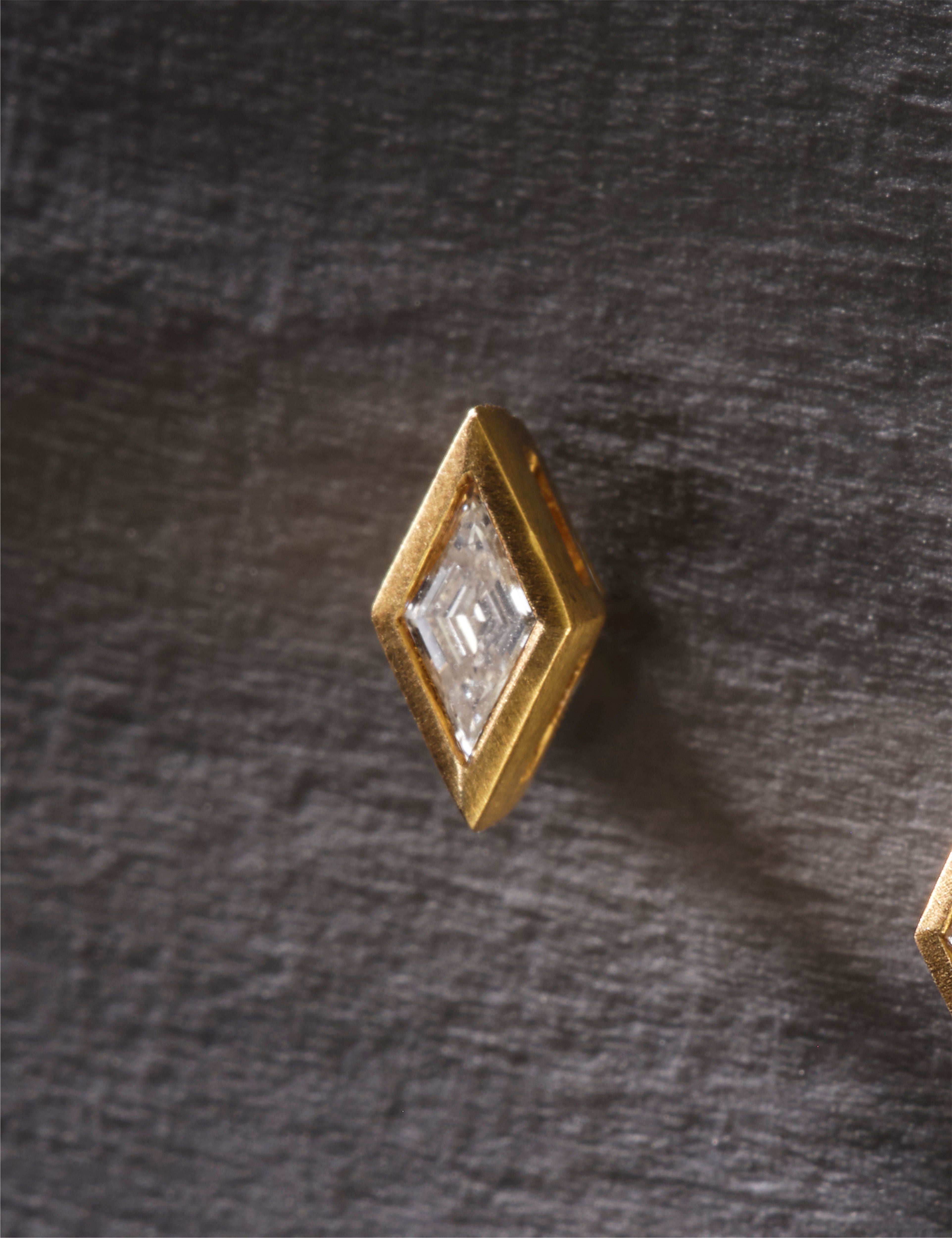 Gold geometric earrings with clear gemstones on a white background.