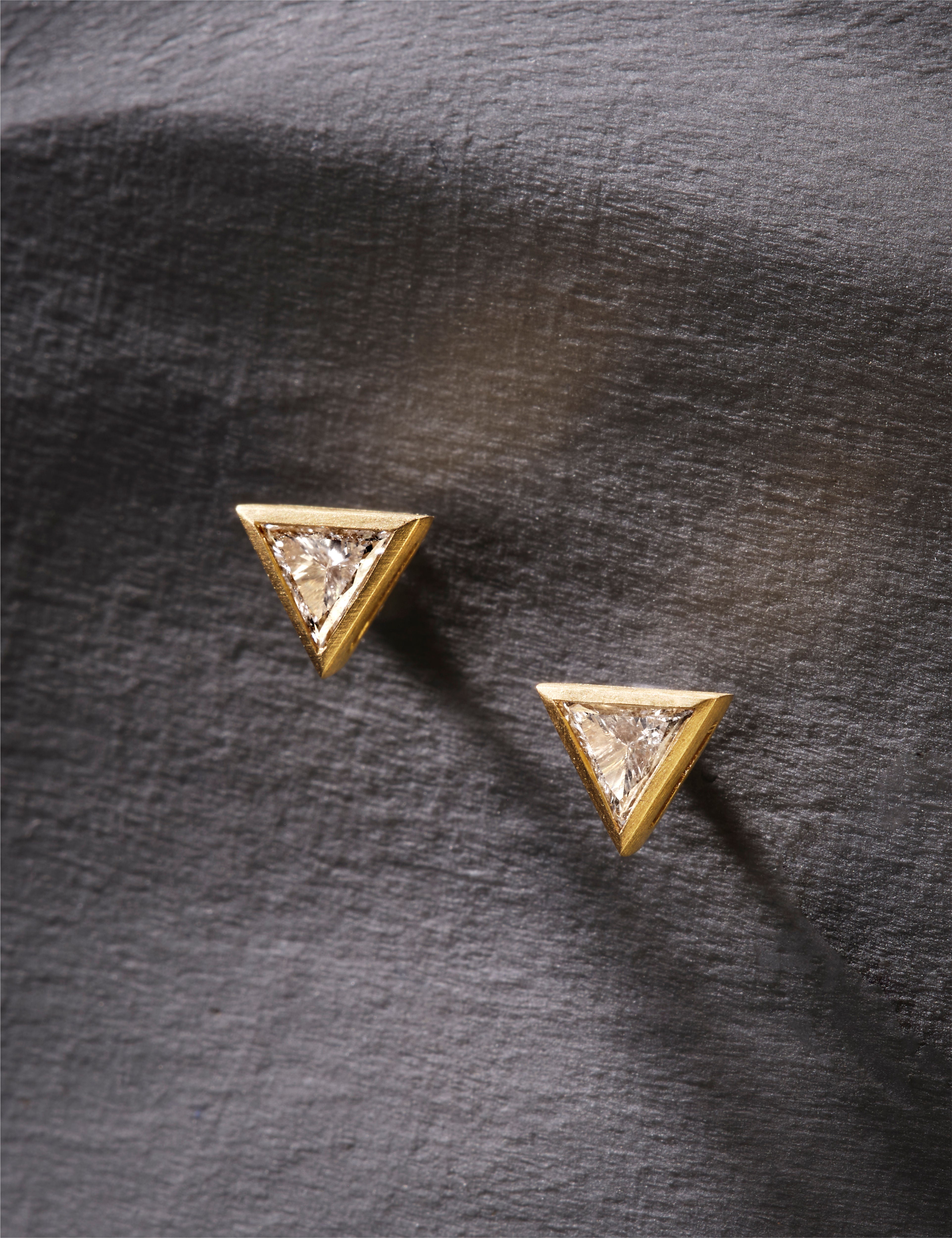 Close-up of a woman wearing gold earrings and a ring, with a neutral background.