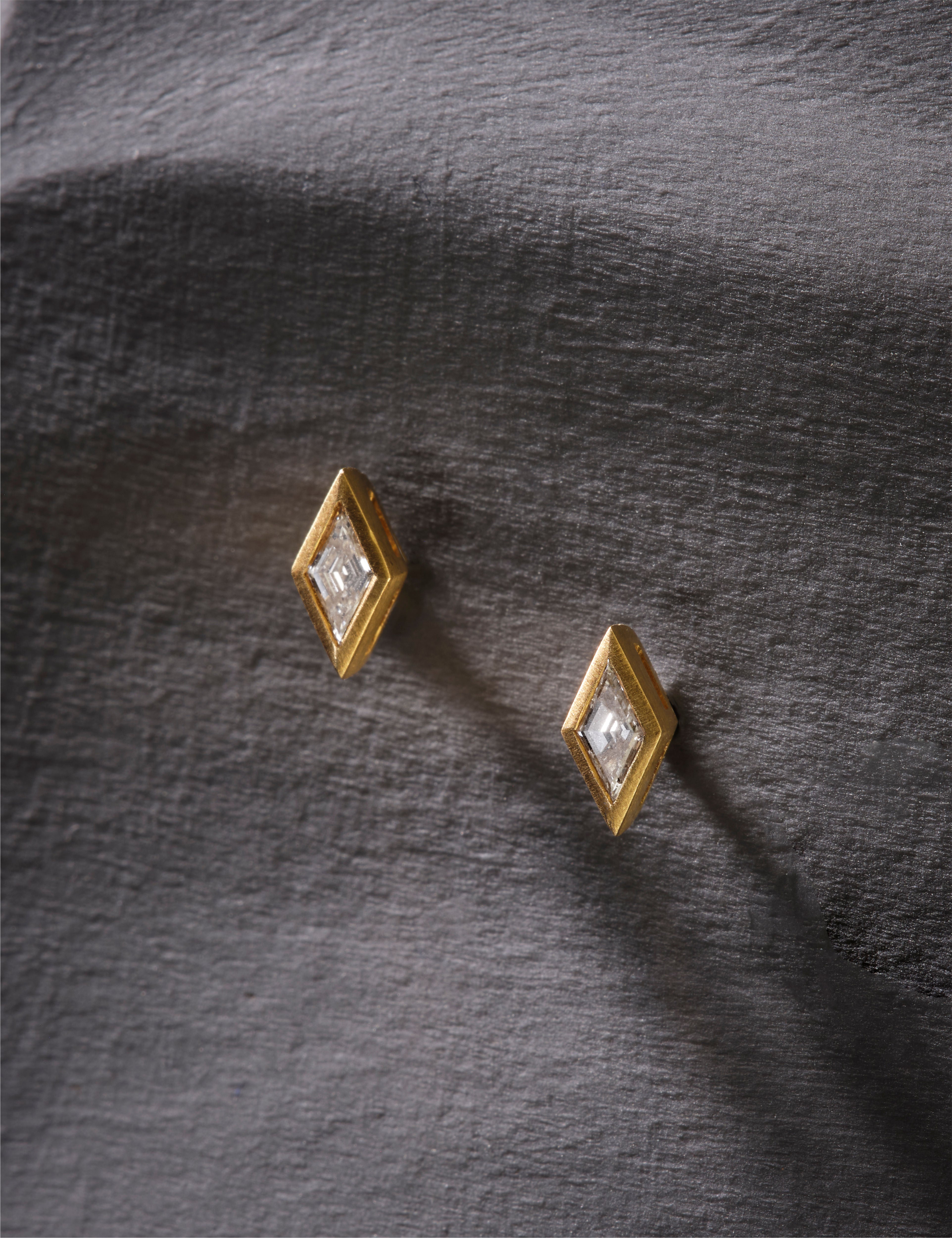 Gold geometric earrings with clear gemstones on a white background.