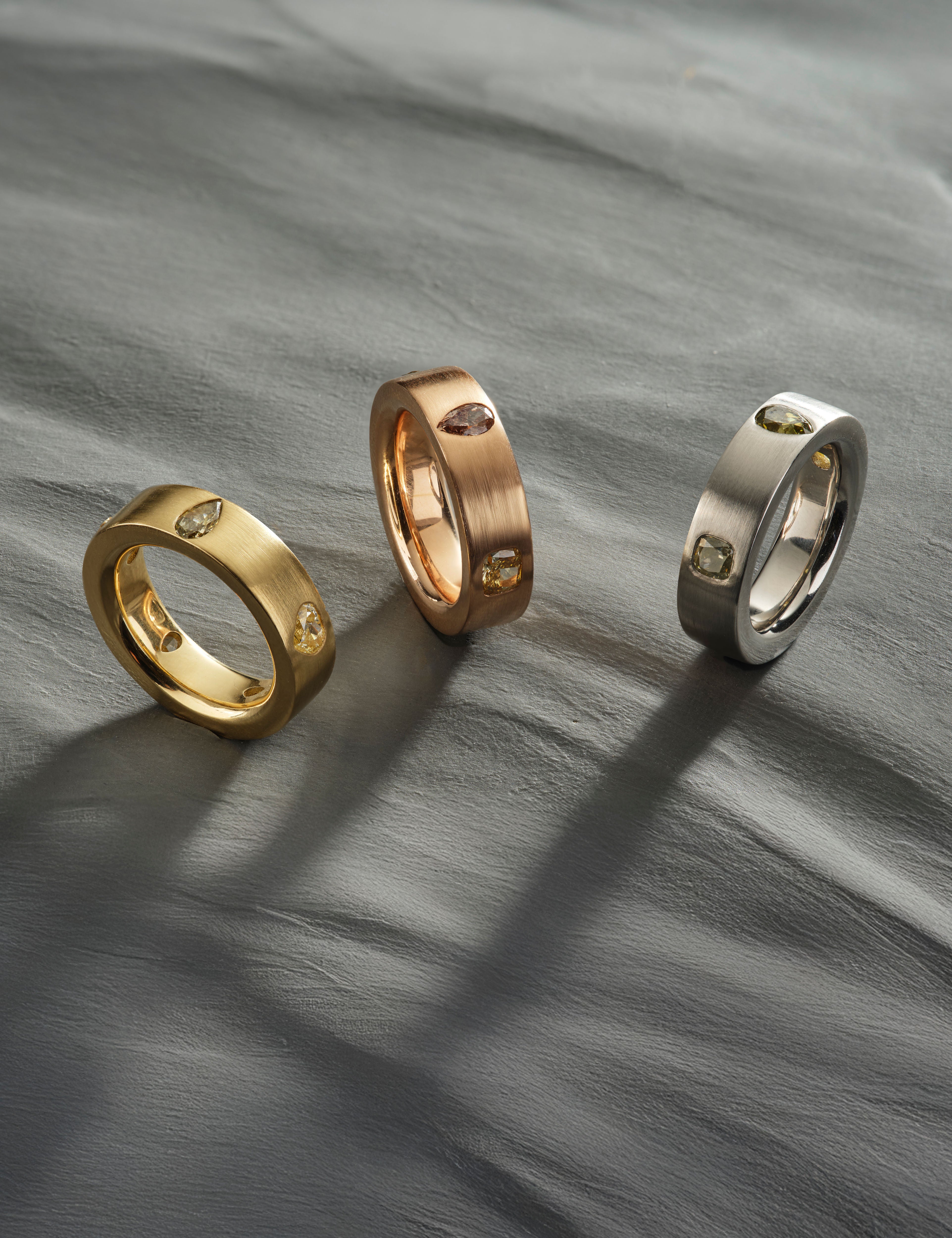 Gold, rose gold, and silver diamond rings displayed on textured grey background.