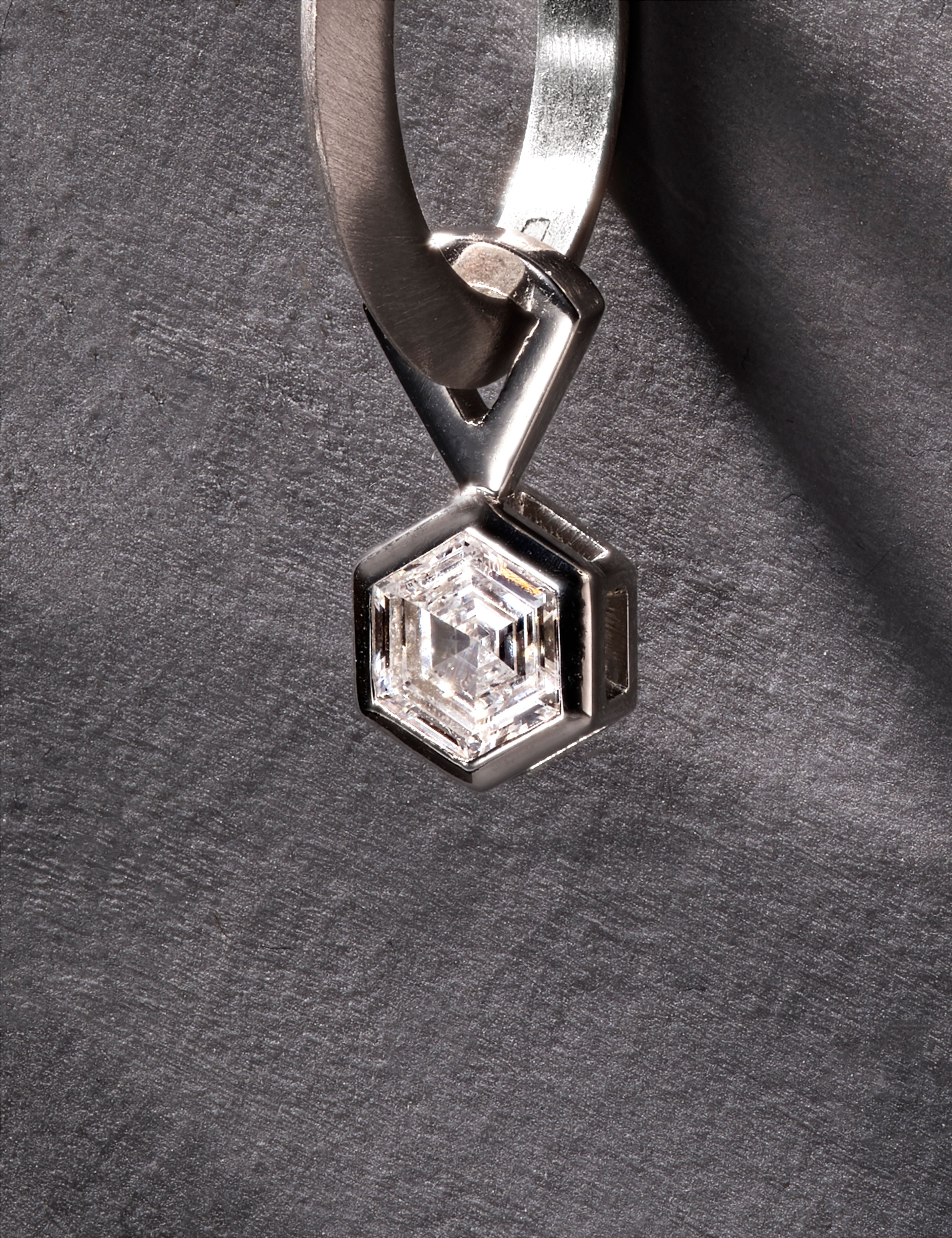 Close-up of platinum hoop earring with hexagon-cut diamond in modern setting.