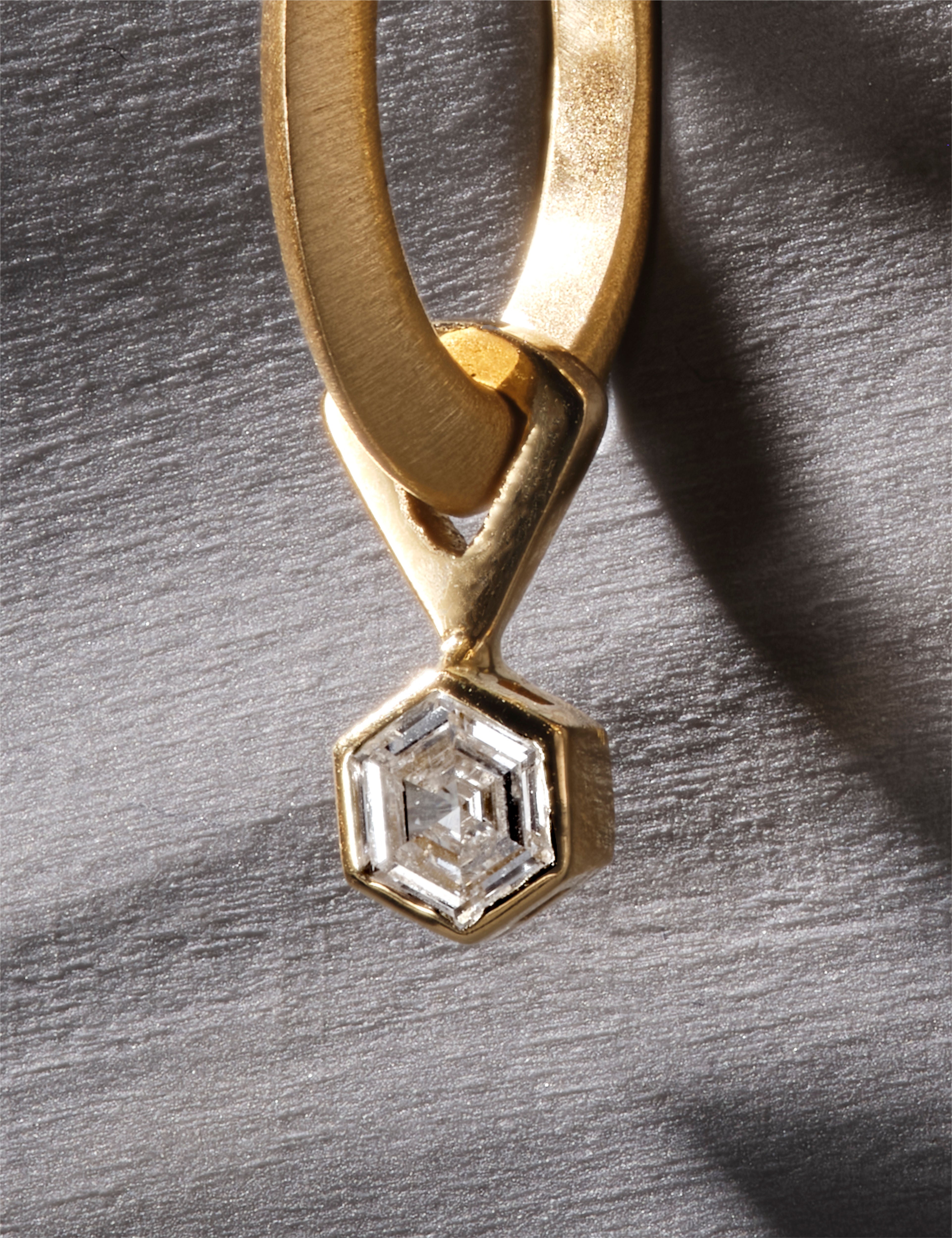 Close-up of yellow gold earring with hexagonal diamond in modern bezel setting.
