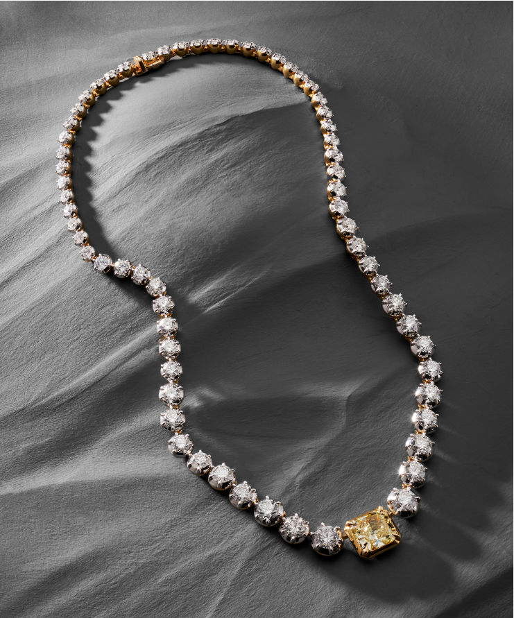 Diamond necklace with a yellow gemstone on a gray fabric background.