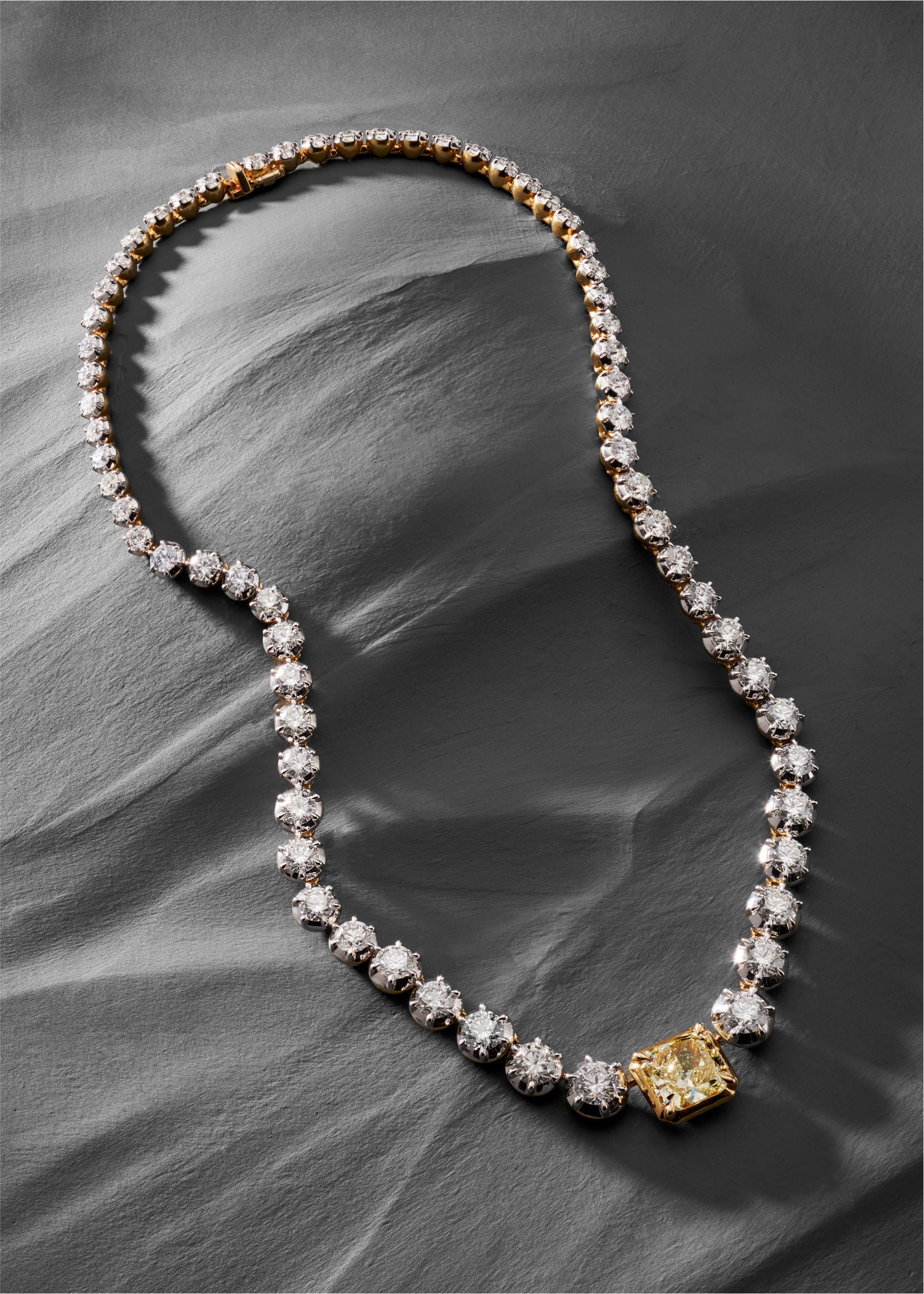 Diamond necklace with a yellow gemstone on a gray fabric background.