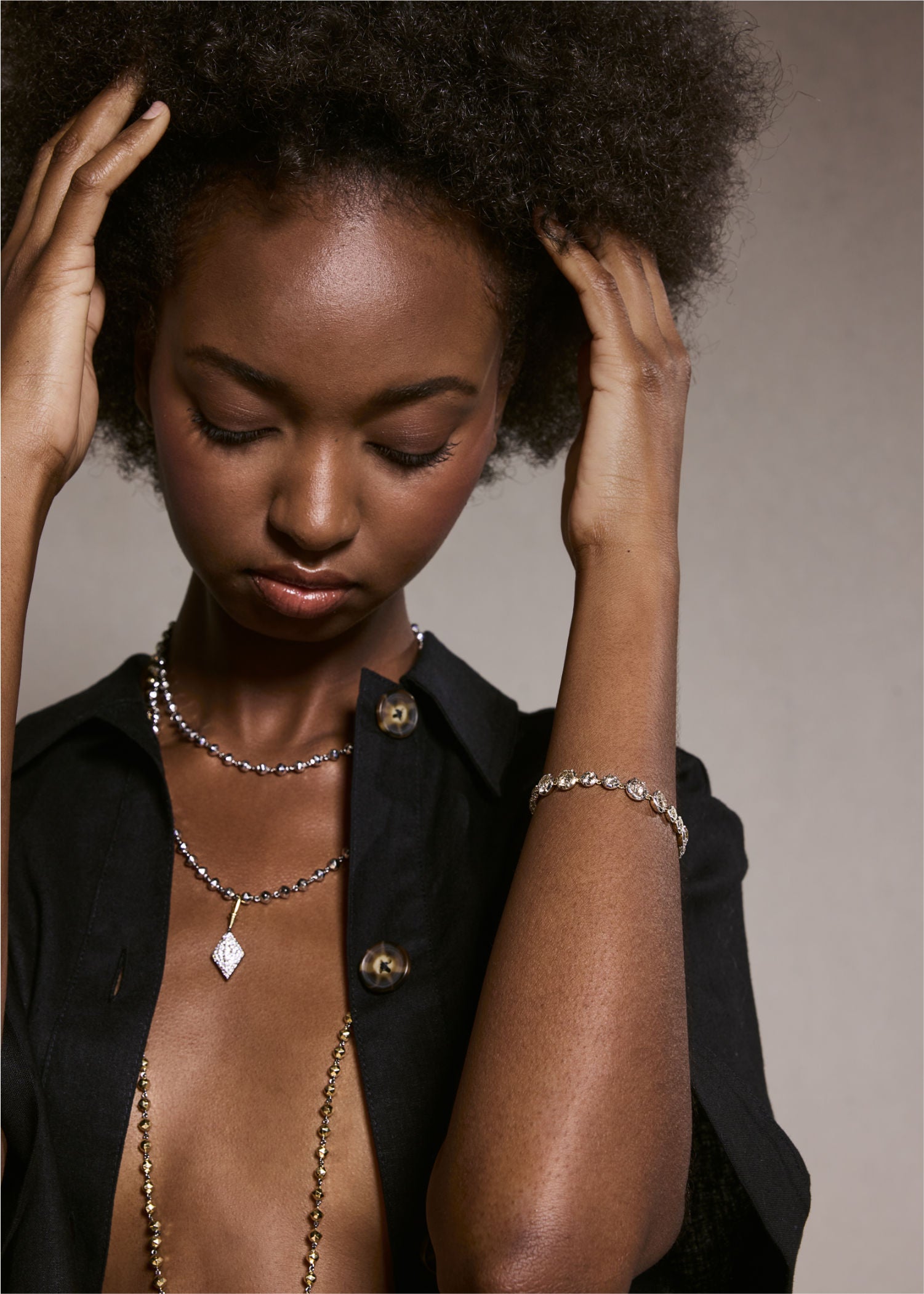 Model wearing a gold diamond tennis bracelet paired with layered gold necklaces featuring bead and diamond pendants.