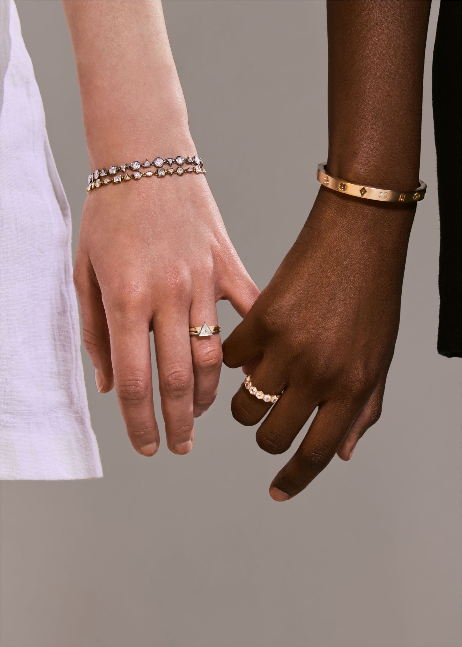 Two people holding hands wearing gold and diamond bracelets and rings.