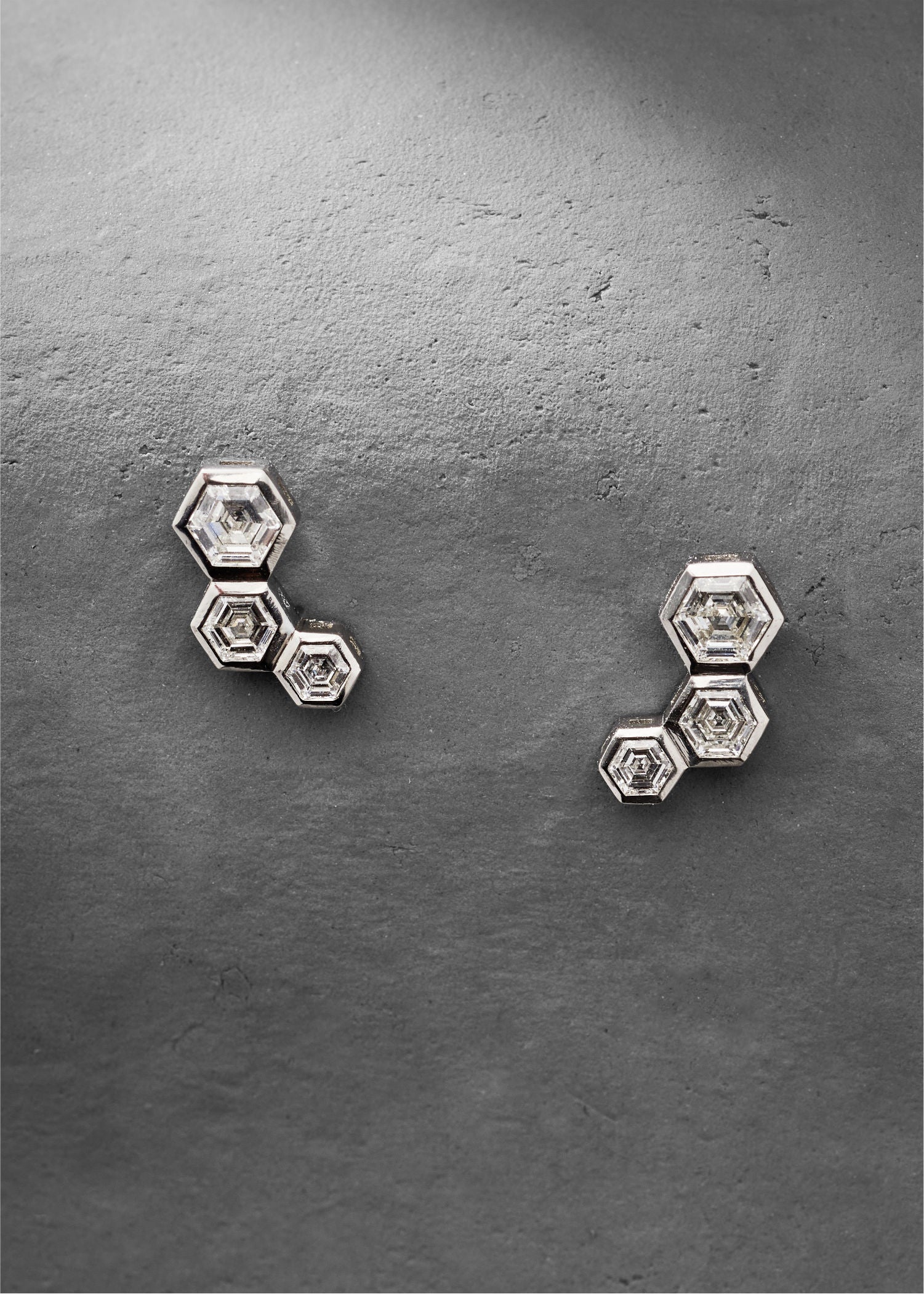 Hexagon diamond stud earrings displayed on textured grey background.
