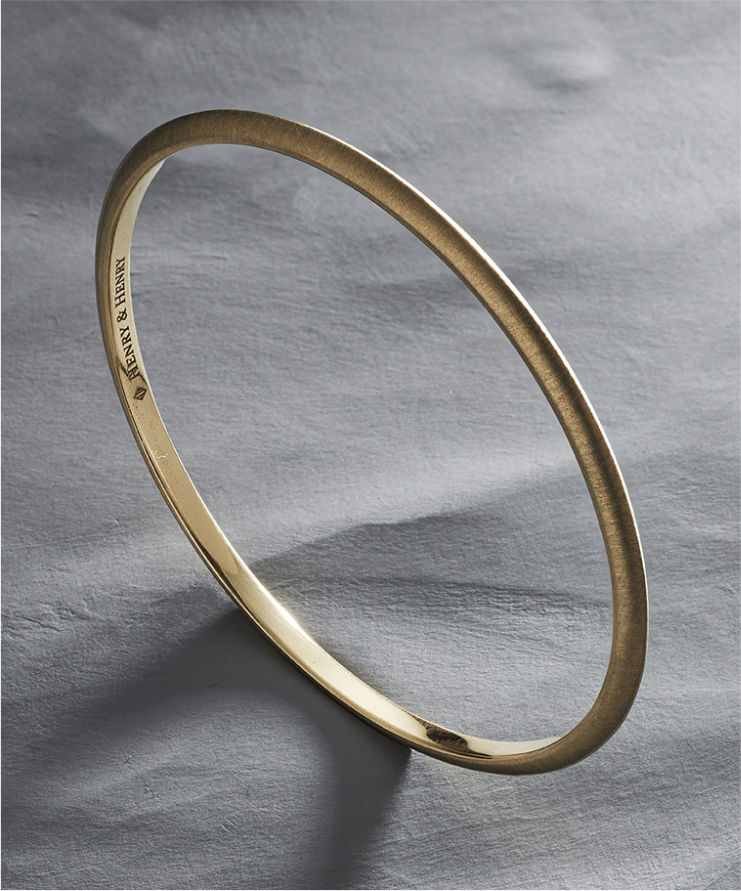 Yellow gold bracelet on a textured gray surface.