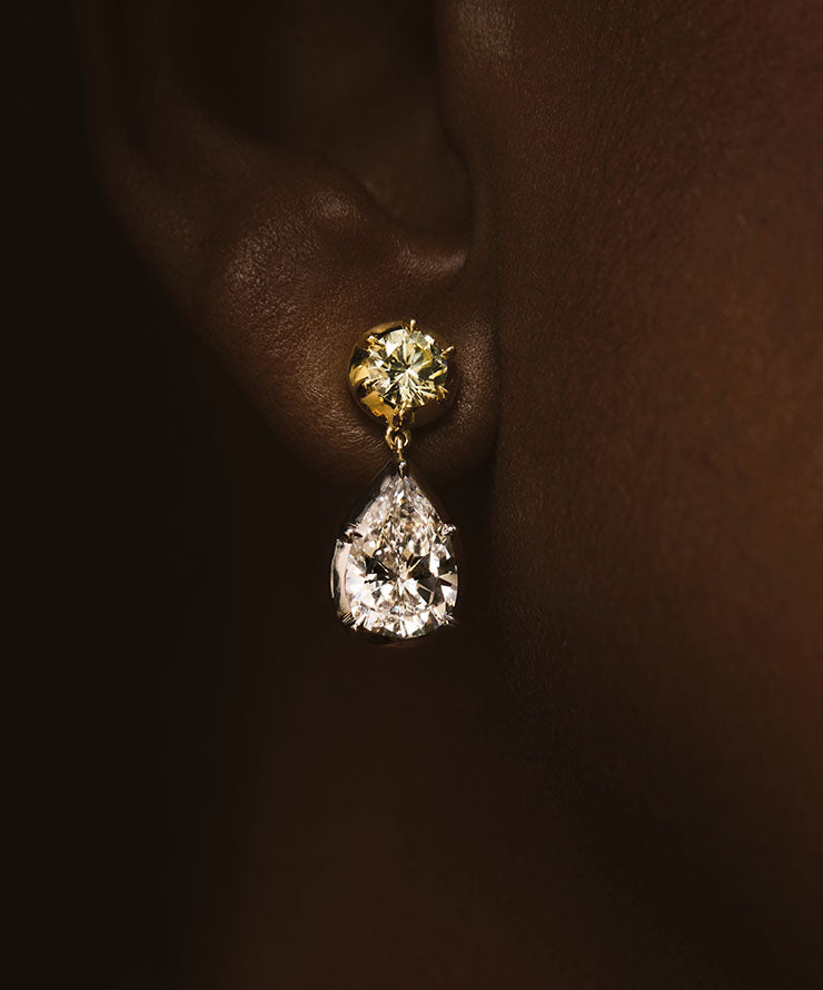 Diamond earring worn on an ear against a dark background.