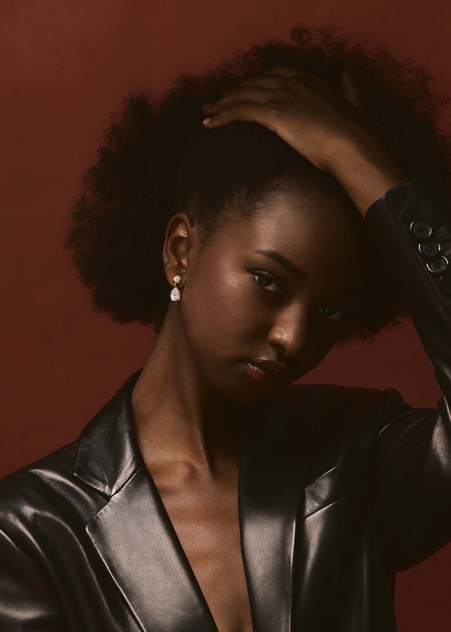 Model wearing gold diamond pear drop earrings with black blazer against warm background.