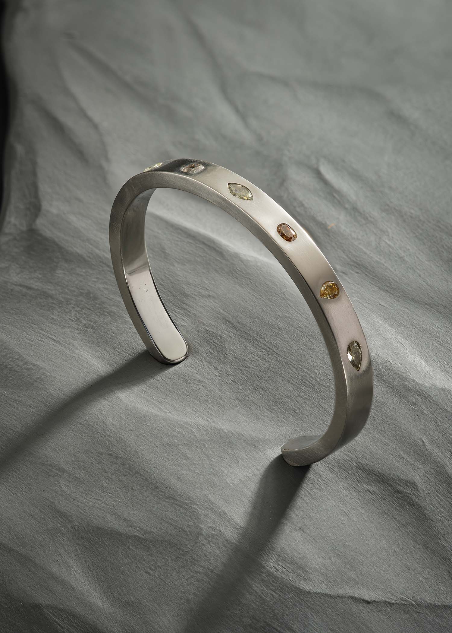 Platinum cuff bracelet with mixed fancy-cut diamonds on matte textured surface.