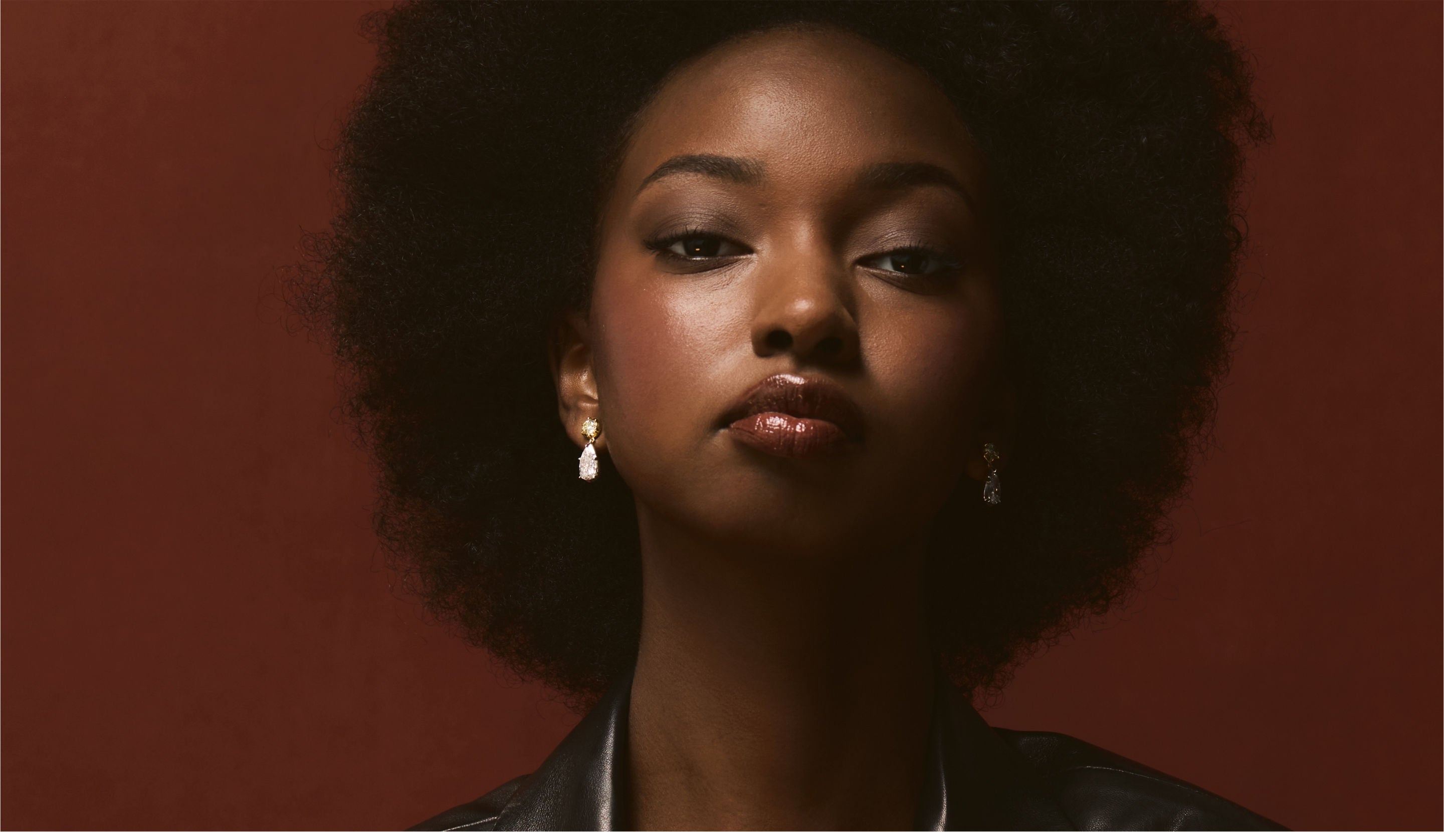 Blonde woman with slicked-back hair wearing a black strapless top and a choker necklace with a large light blue gemstone.
