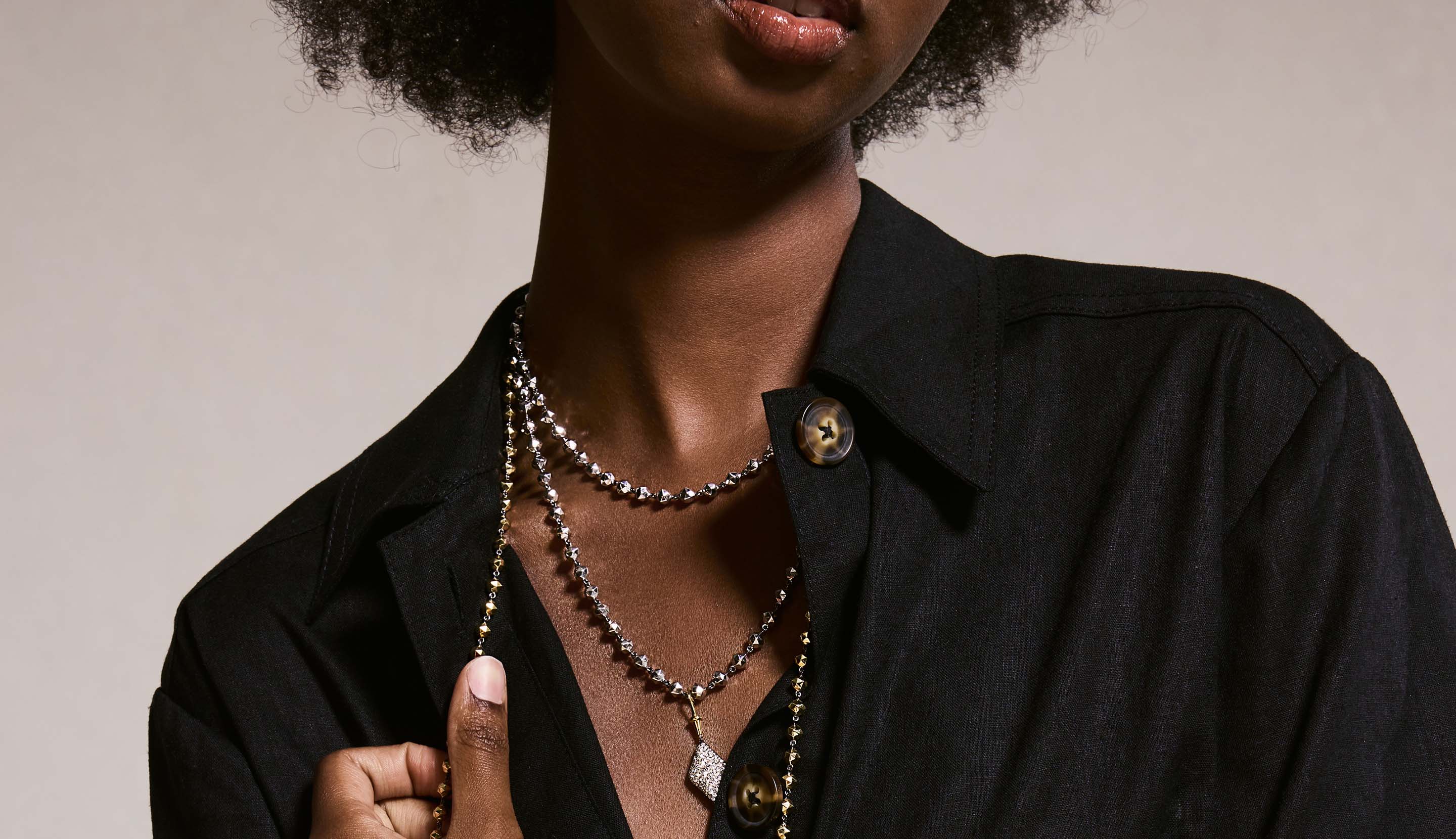 Blonde woman with slicked-back hair wearing a black strapless top and a choker necklace with a large light blue gemstone.