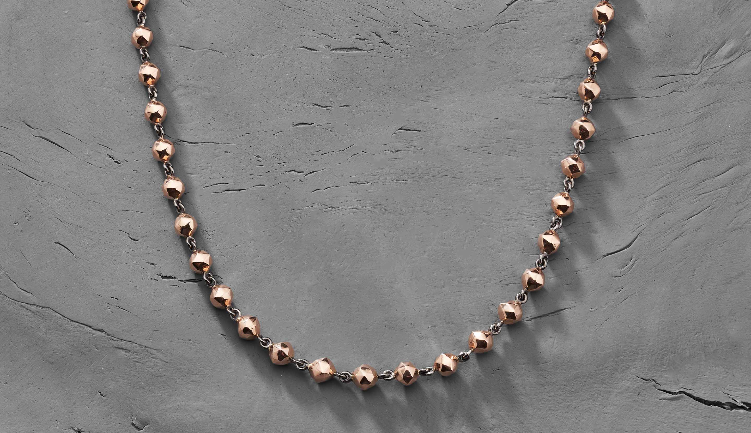 Blonde woman with slicked-back hair wearing a black strapless top and a choker necklace with a large light blue gemstone.