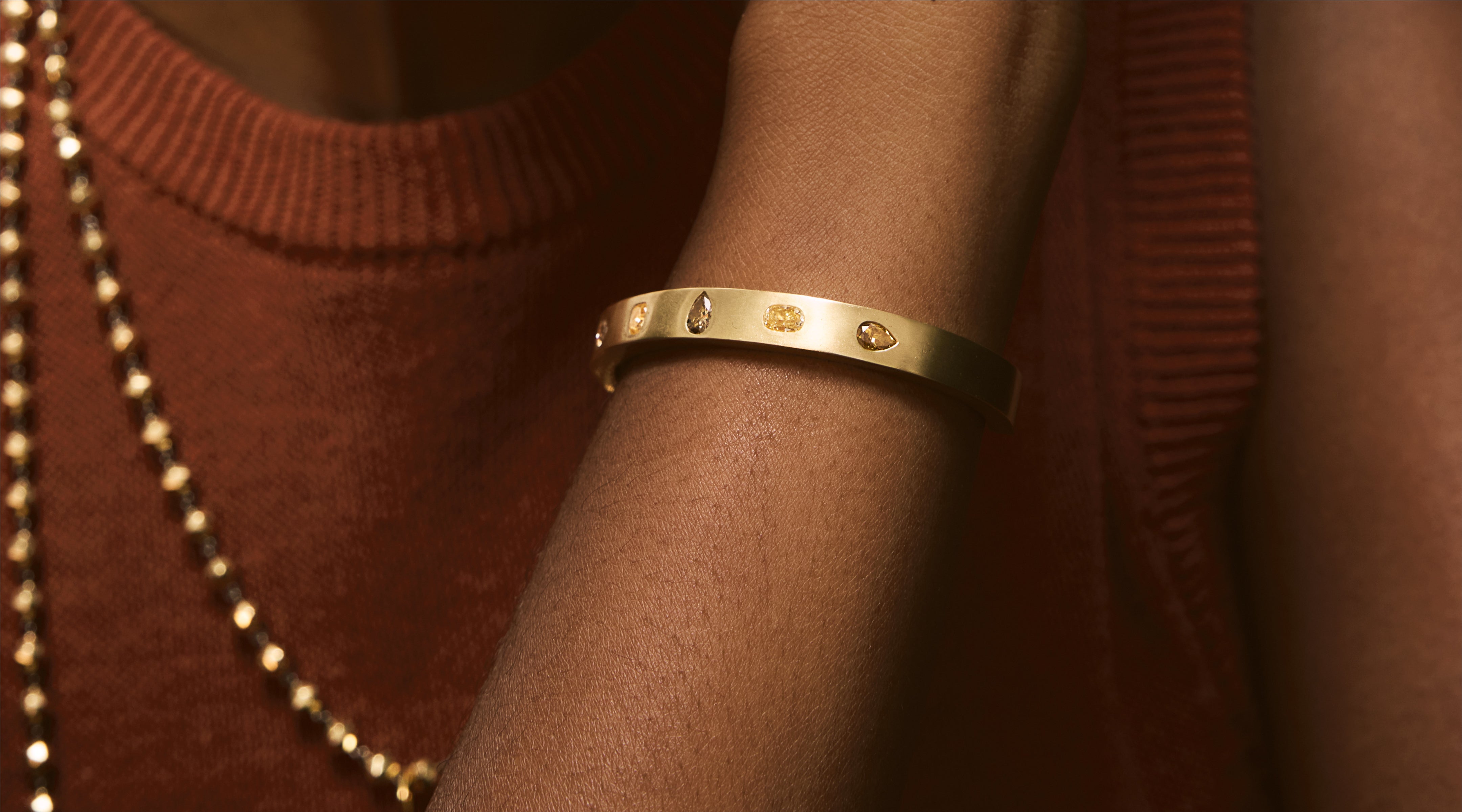 Blonde woman with slicked-back hair wearing a black strapless top and a choker necklace with a large light blue gemstone.