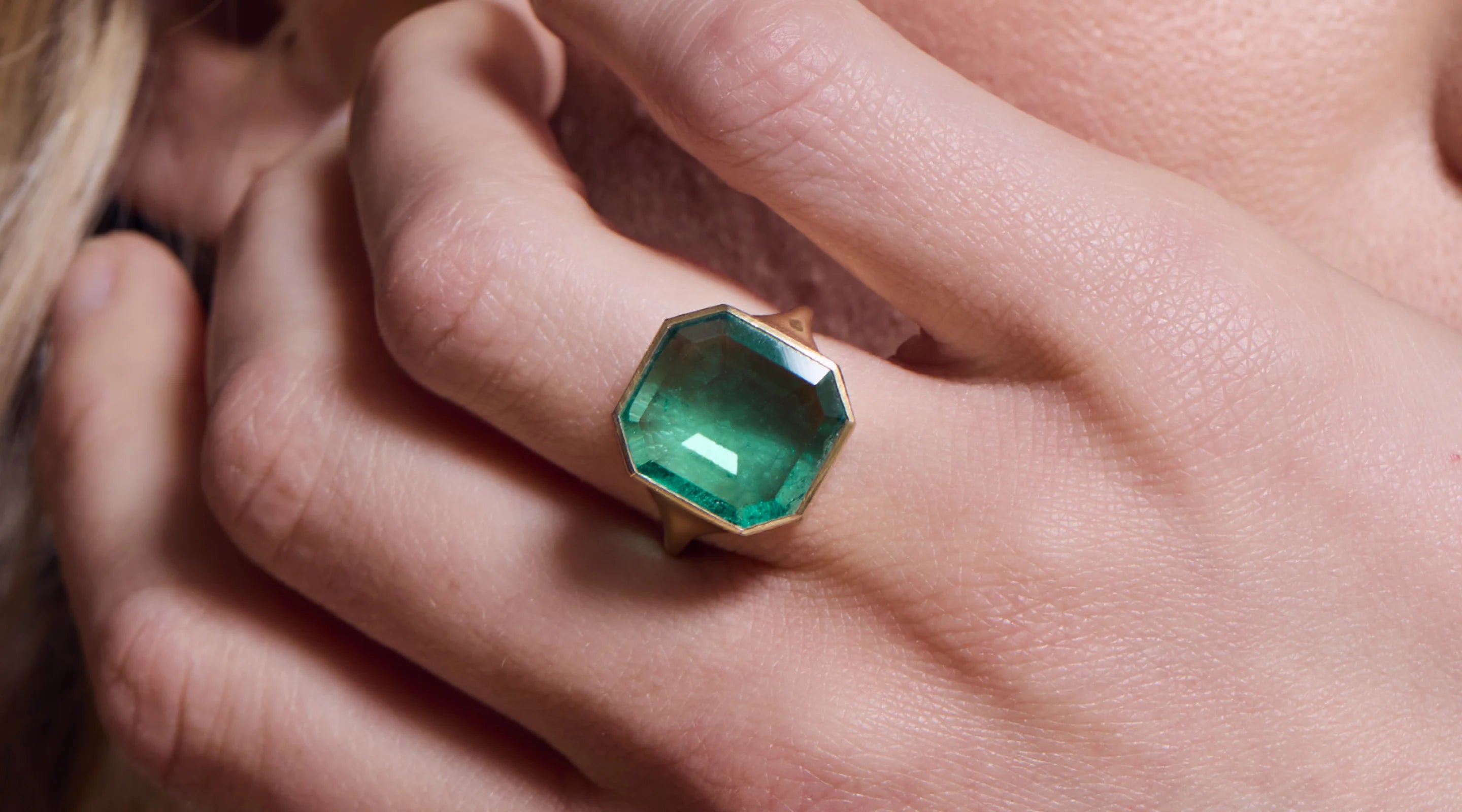 Blonde woman with slicked-back hair wearing a black strapless top and a choker necklace with a large light blue gemstone.