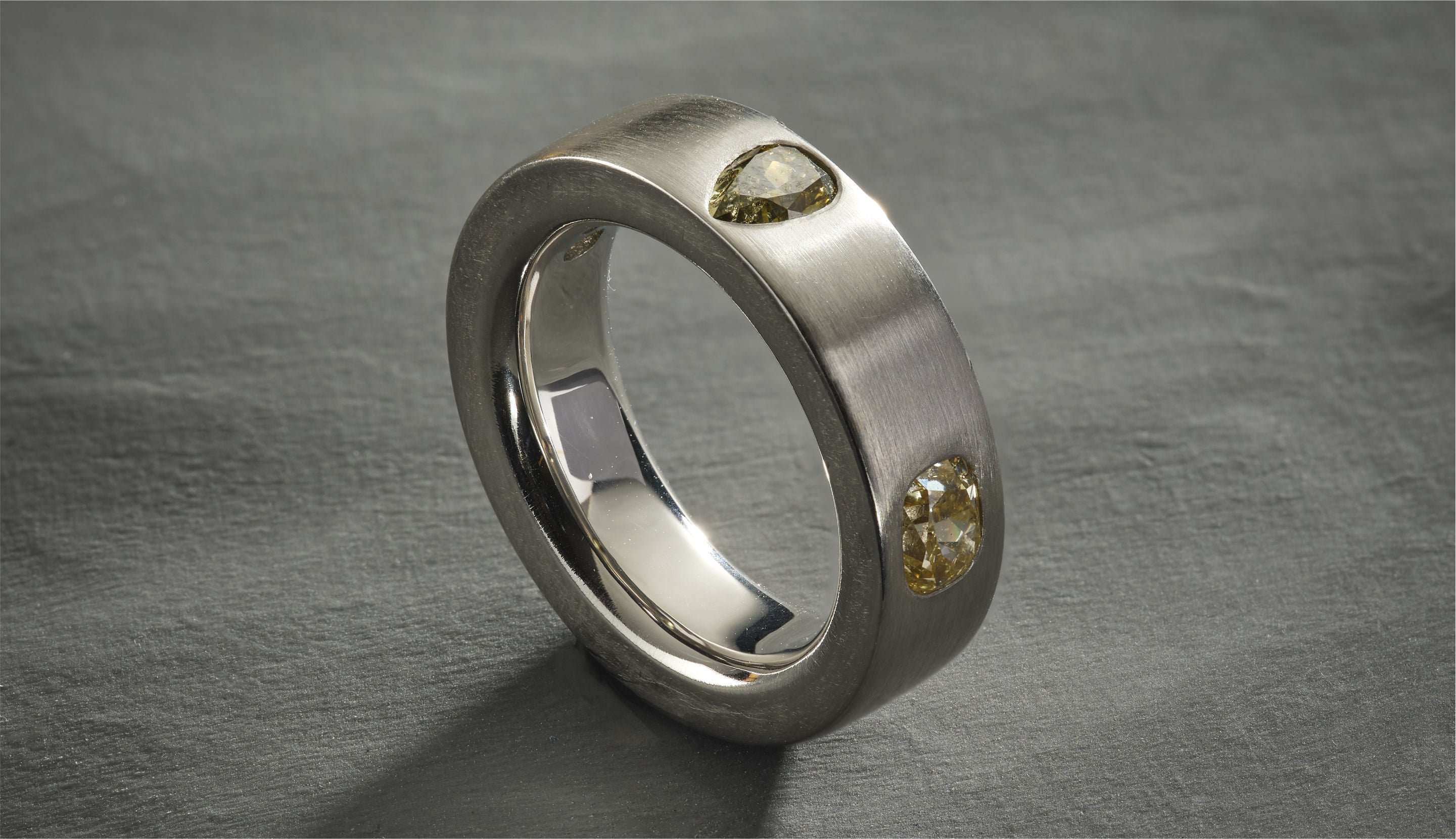 Blonde woman with slicked-back hair wearing a black strapless top and a choker necklace with a large light blue gemstone.