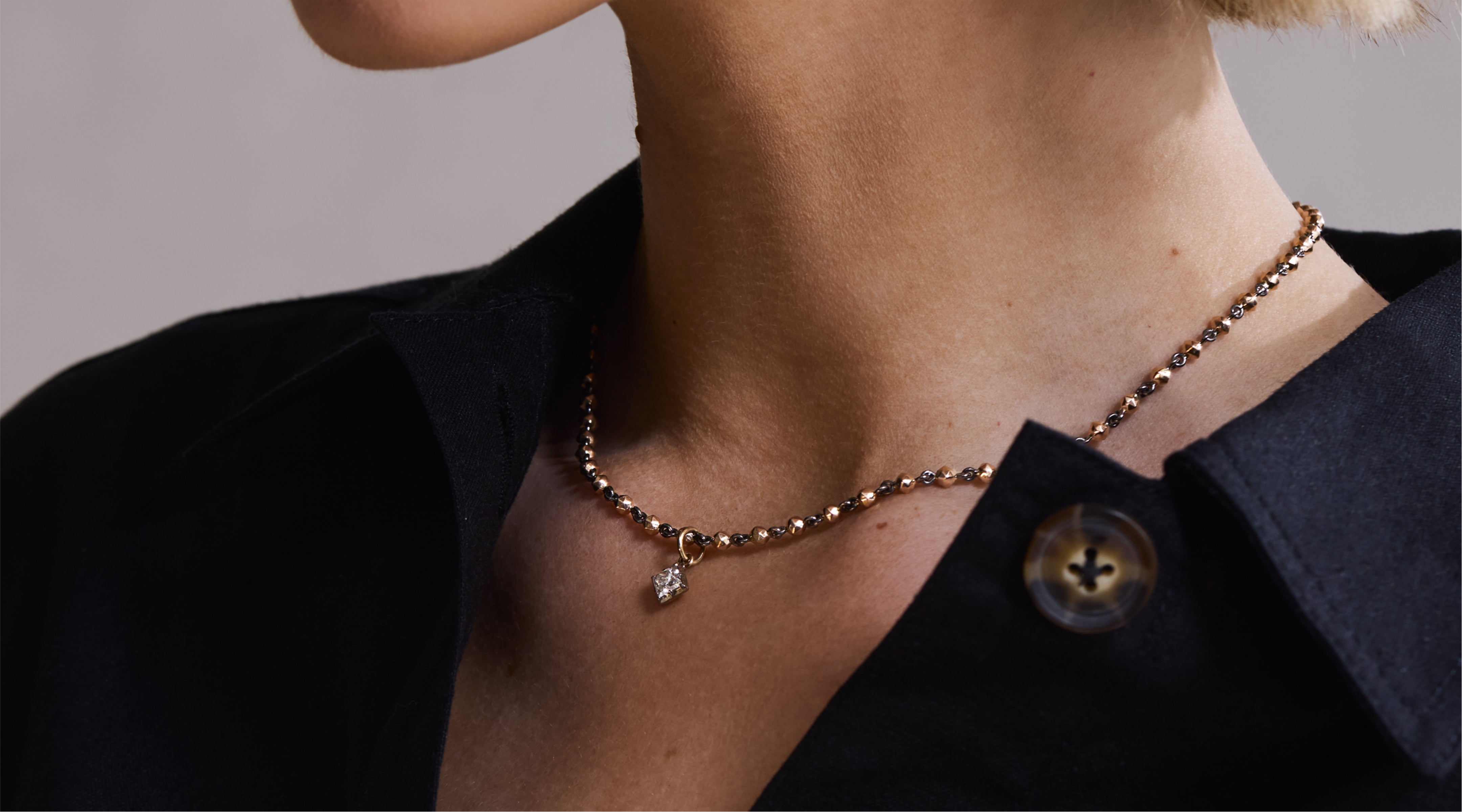 Blonde woman with slicked-back hair wearing a black strapless top and a choker necklace with a large light blue gemstone.