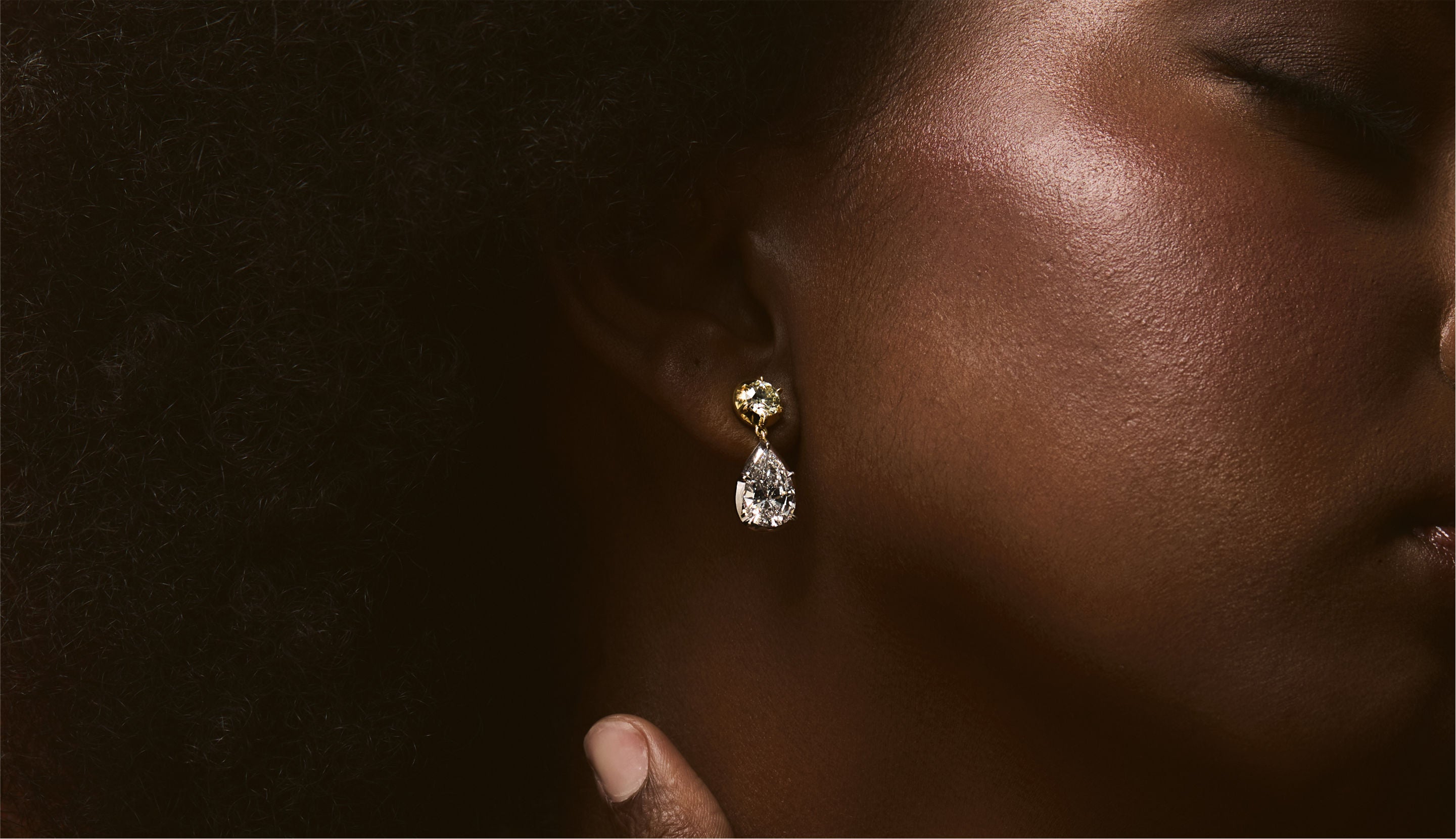 Blonde woman with slicked-back hair wearing a black strapless top and a choker necklace with a large light blue gemstone.