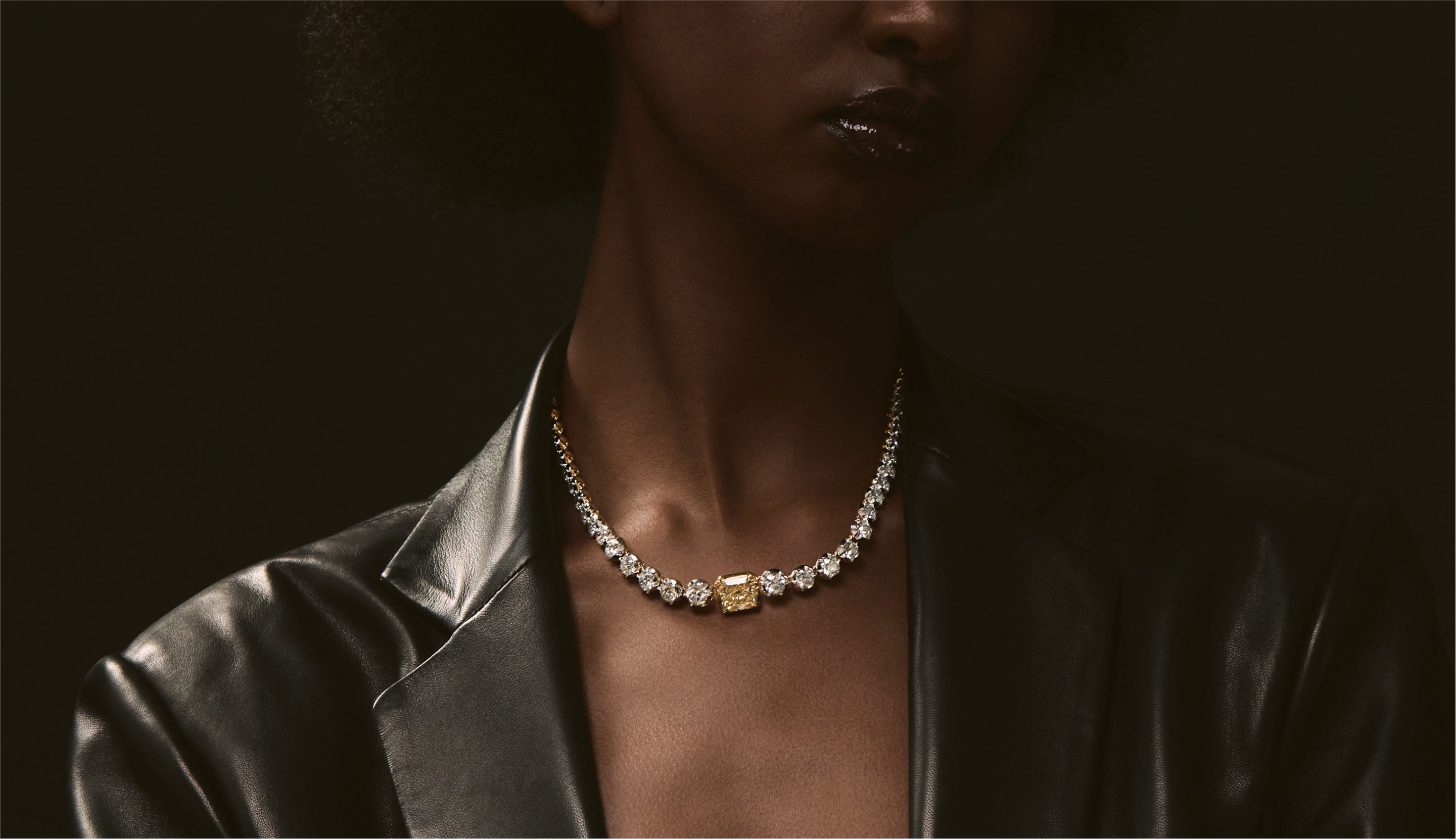 Blonde woman with slicked-back hair wearing a black strapless top and a choker necklace with a large light blue gemstone.