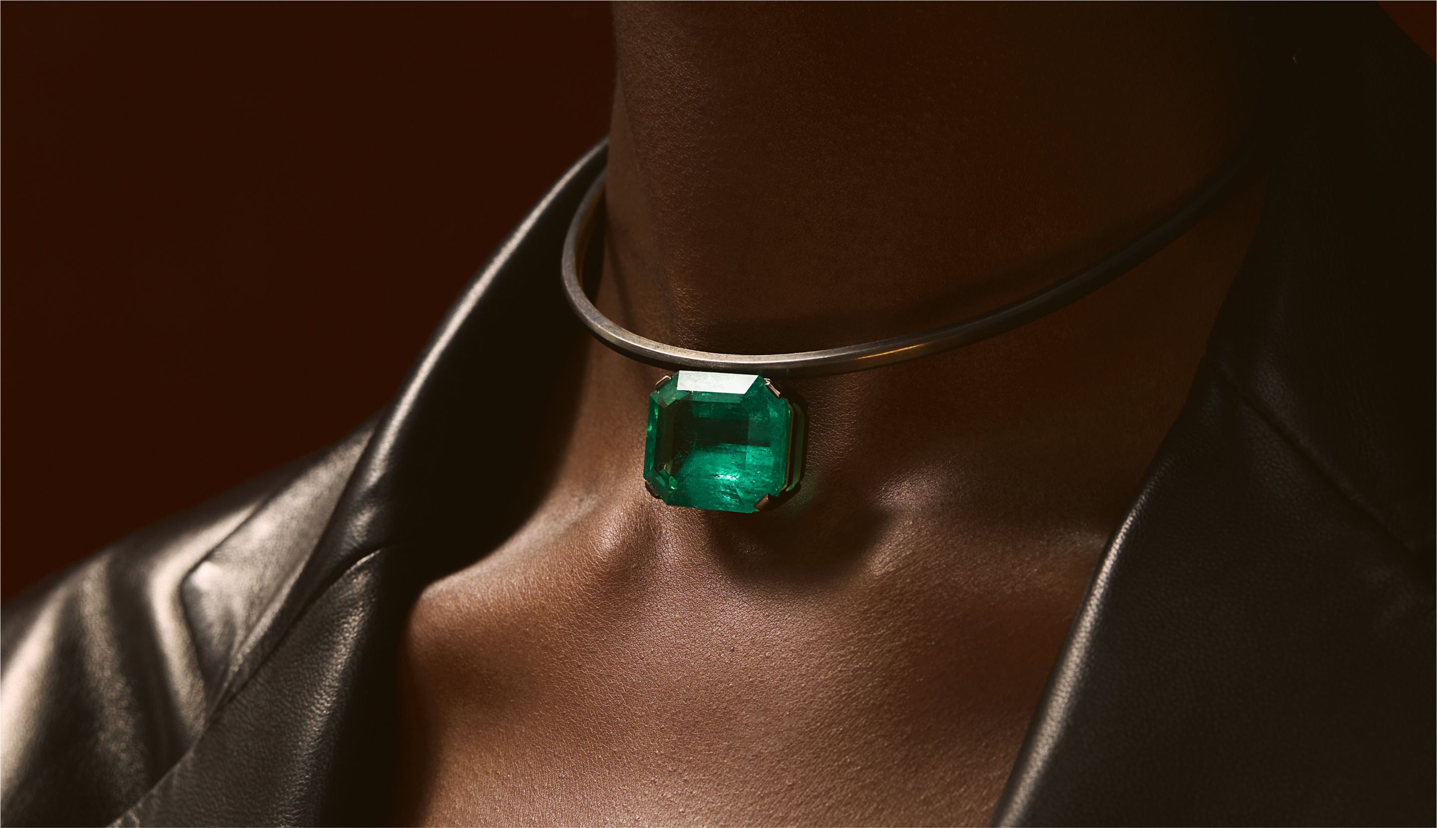 Blonde woman with slicked-back hair wearing a black strapless top and a choker necklace with a large light blue gemstone.