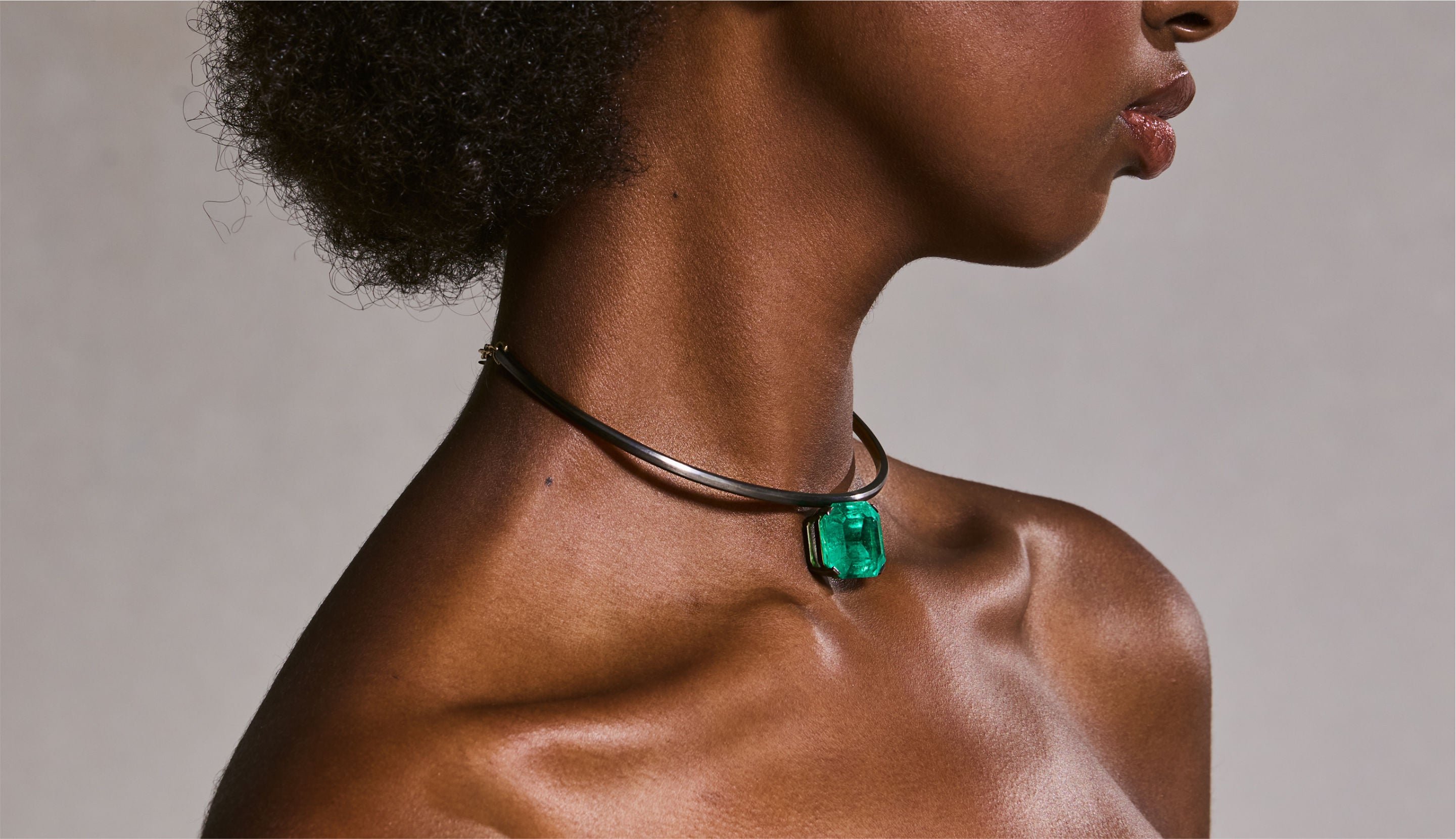 Blonde woman with slicked-back hair wearing a black strapless top and a choker necklace with a large light blue gemstone.