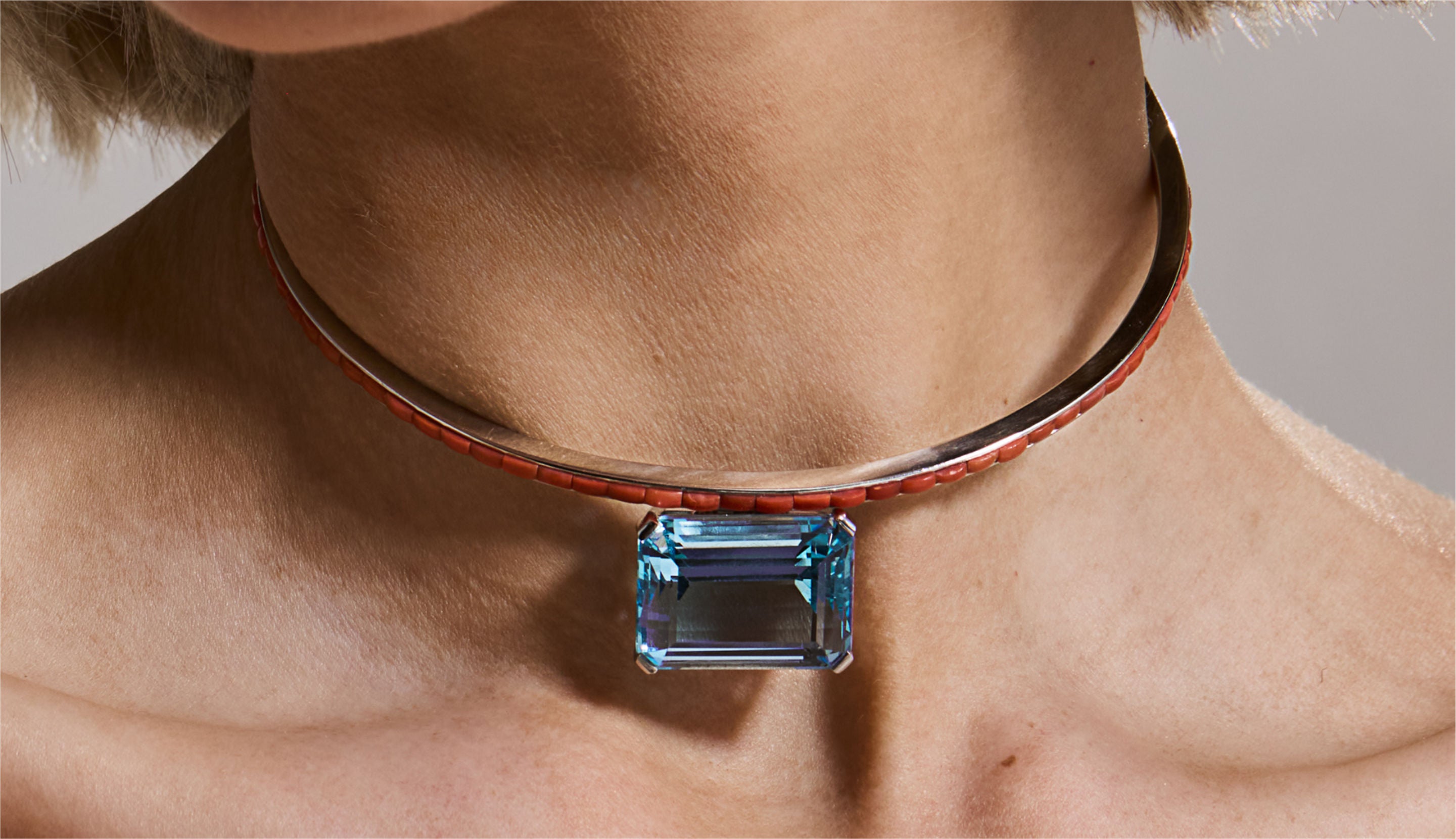 Blonde woman with slicked-back hair wearing a black strapless top and a choker necklace with a large light blue gemstone.