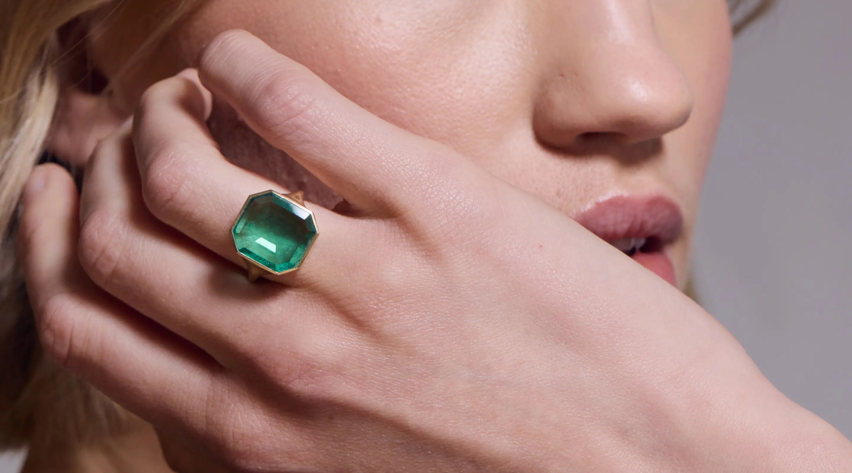 Blonde woman with slicked-back hair wearing a black strapless top and a choker necklace with a large light blue gemstone.