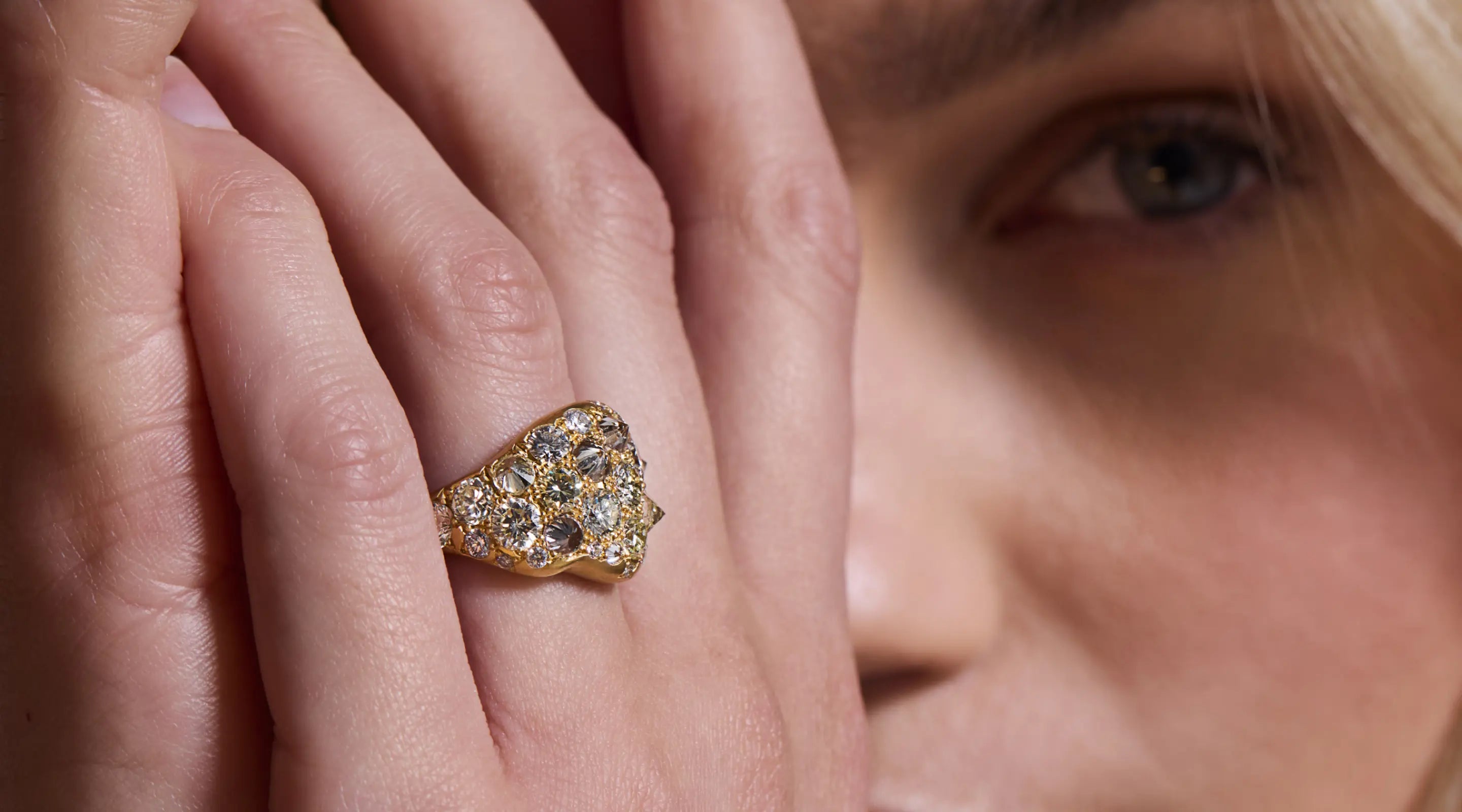 Blonde woman with slicked-back hair wearing a black strapless top and a choker necklace with a large light blue gemstone.